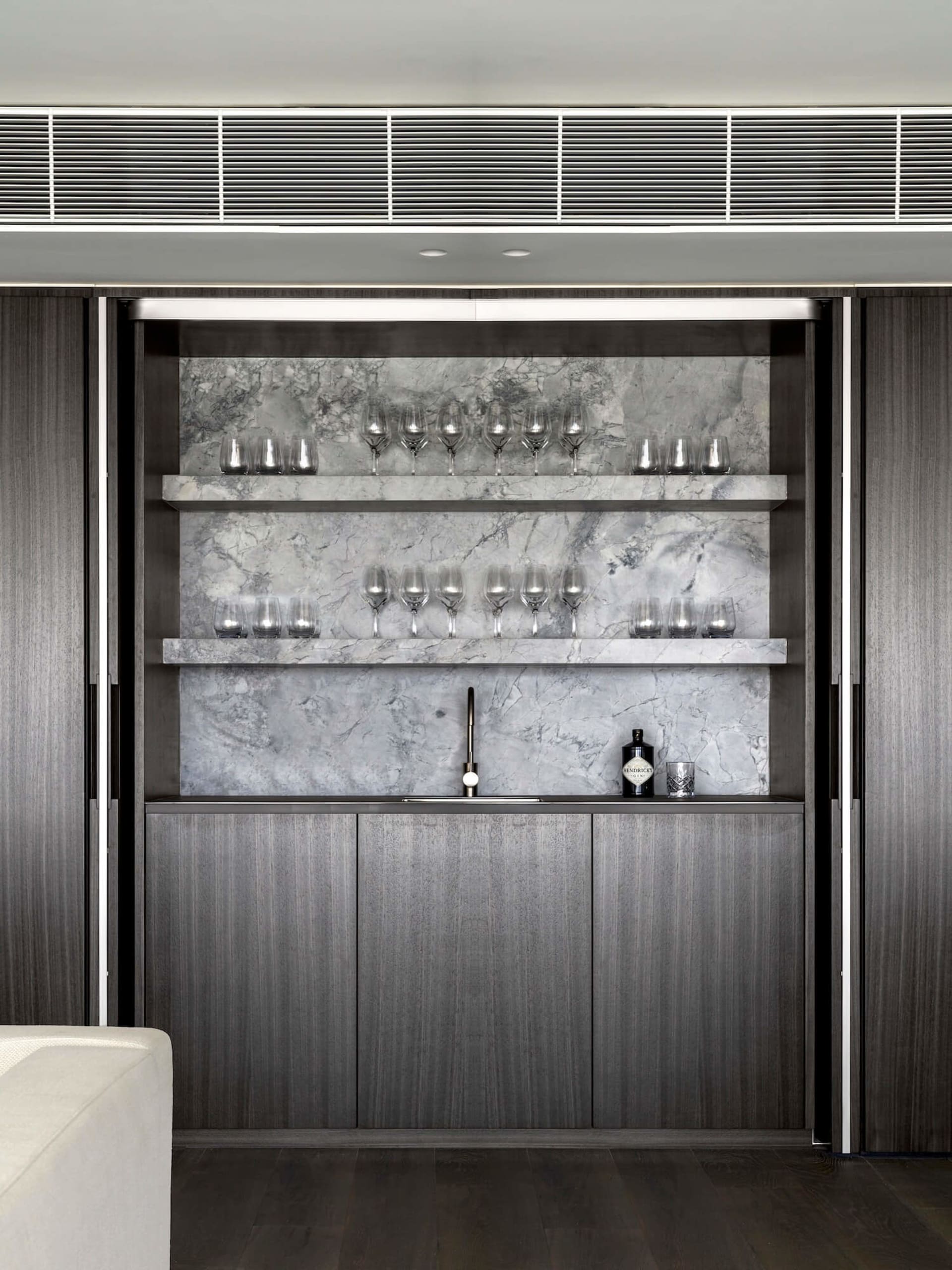 Modern bar area featuring marble countertops and shelves with glasses.