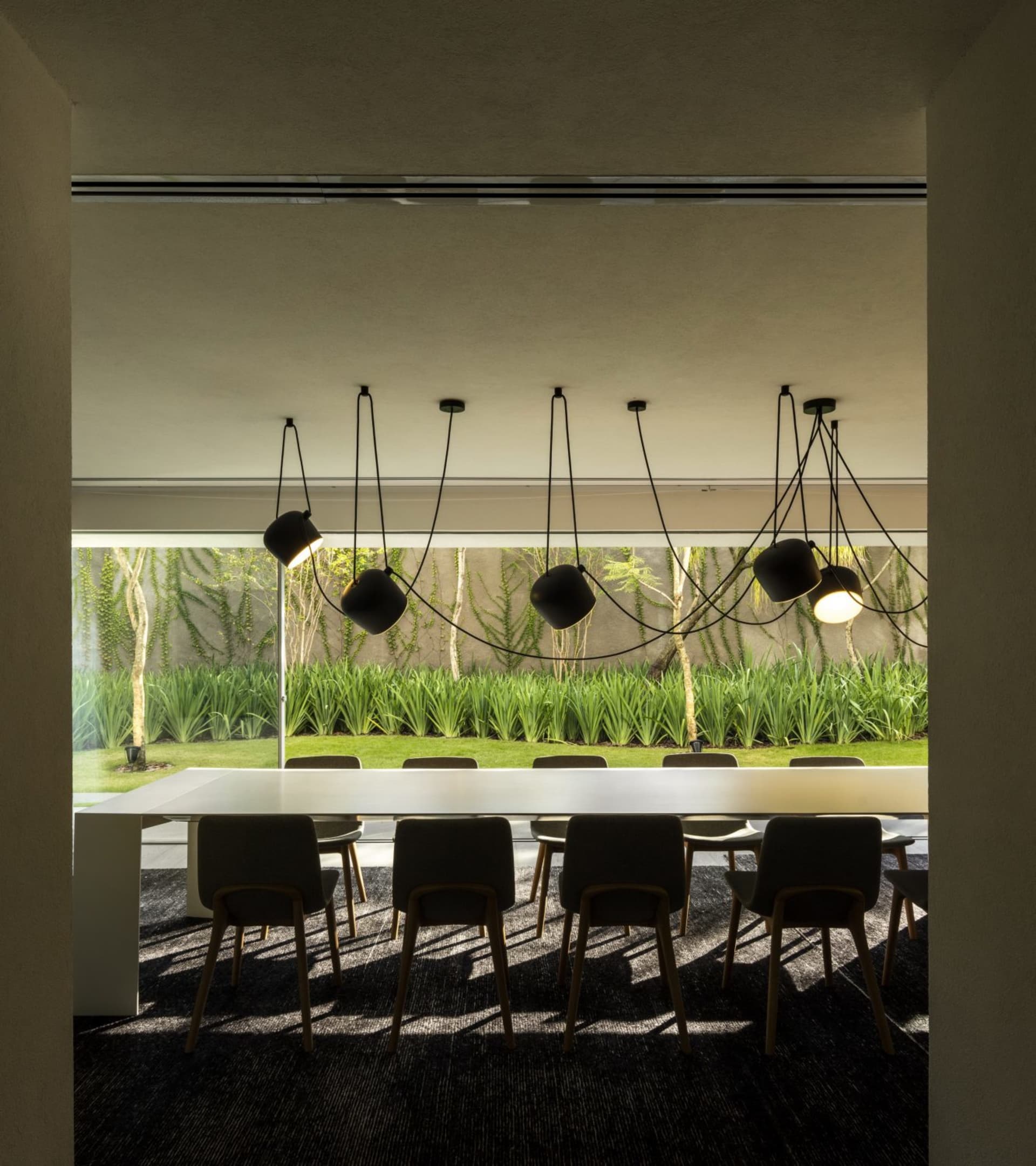 Minimalist dining room with black lighting, concrete floor, and a view of the garden.