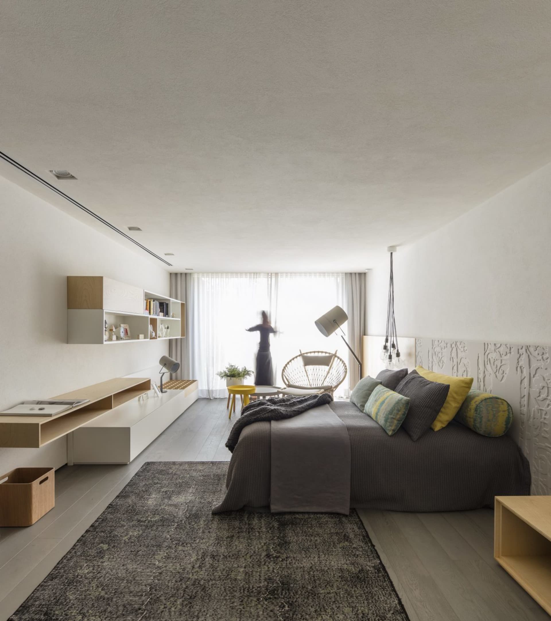 Modern minimalist bedroom with a bed, lamp, and chair near a large window.