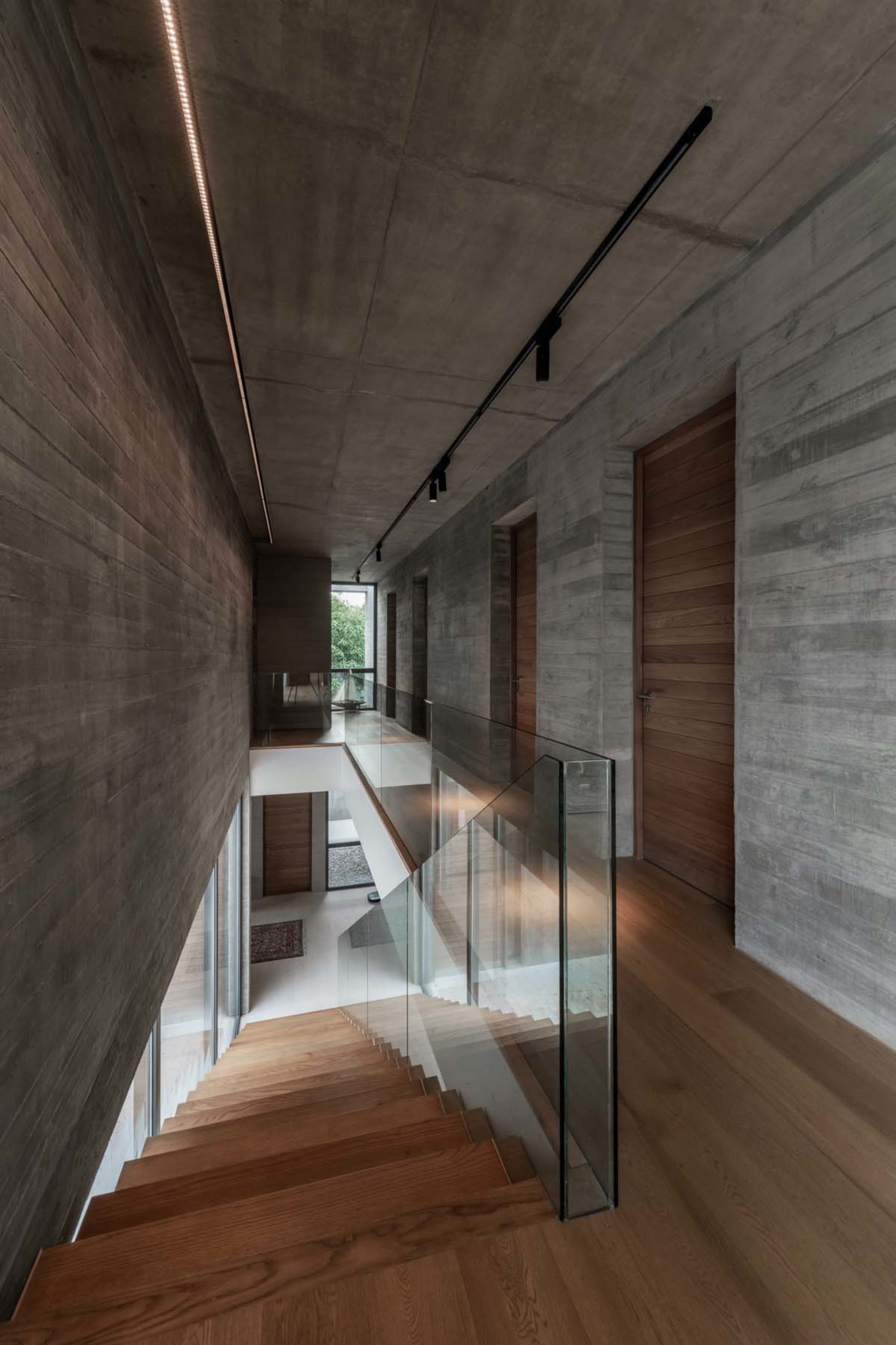 A minimalist home interior with concrete walls, glass railings, and wooden stairs.