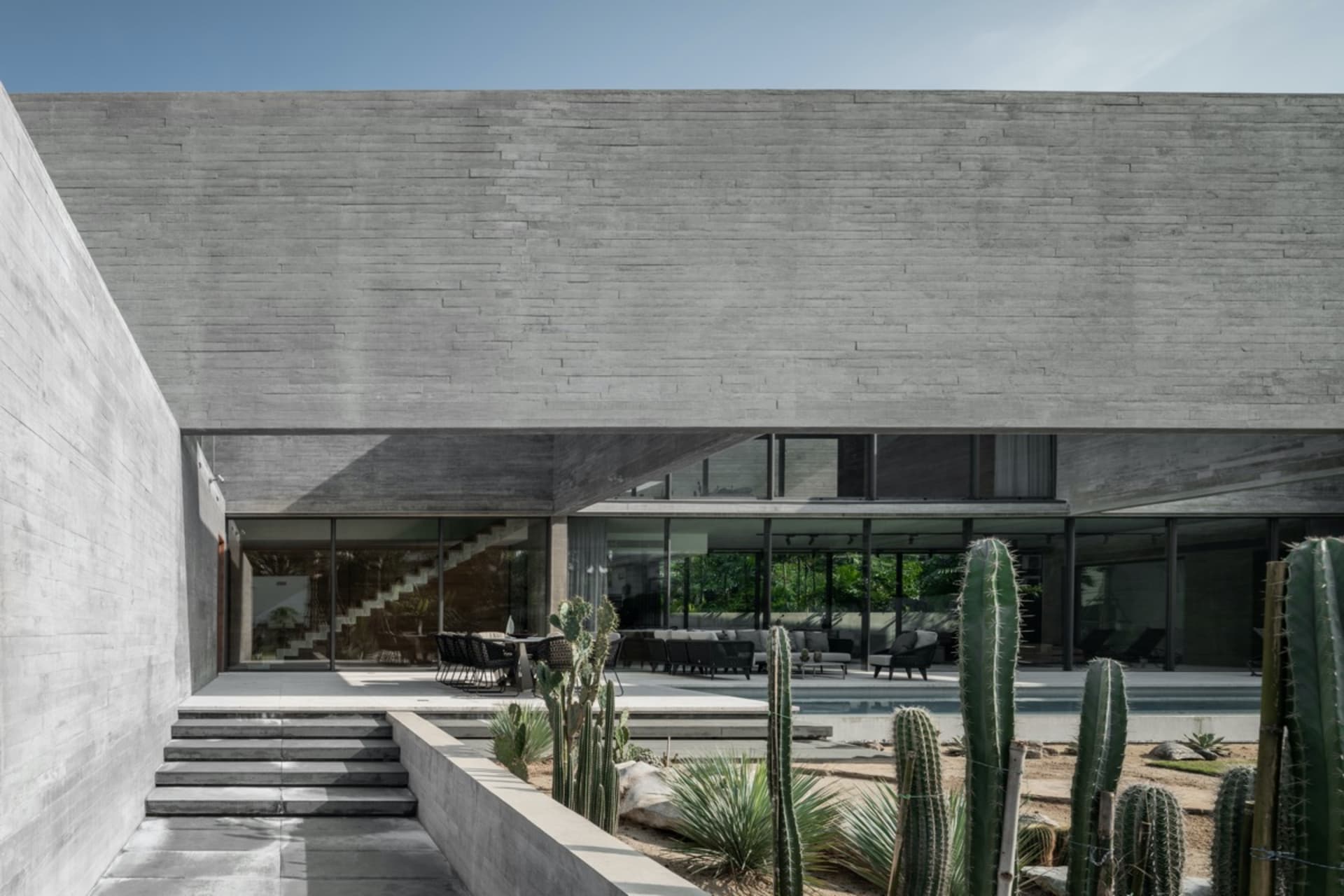 A modern house with a sleek, minimalist design featuring concrete walls and a large patio area with cacti and outdoor furnitu