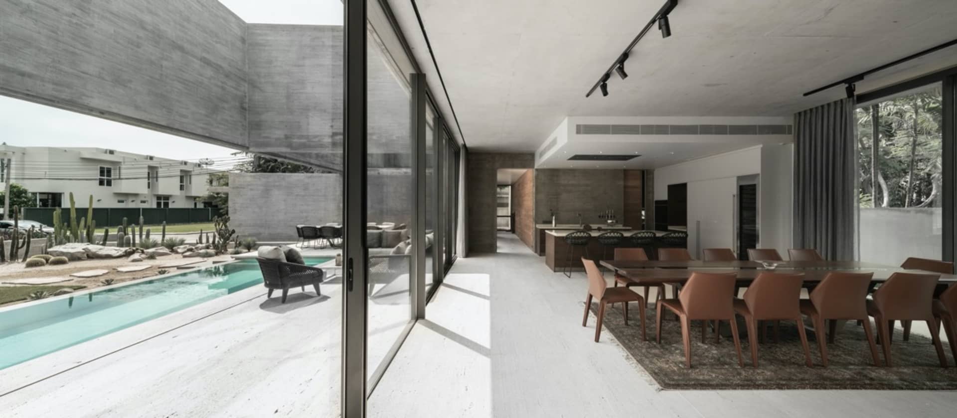 Modern residential interior featuring a concrete dining area with glass and steel accents and a backyard pool.