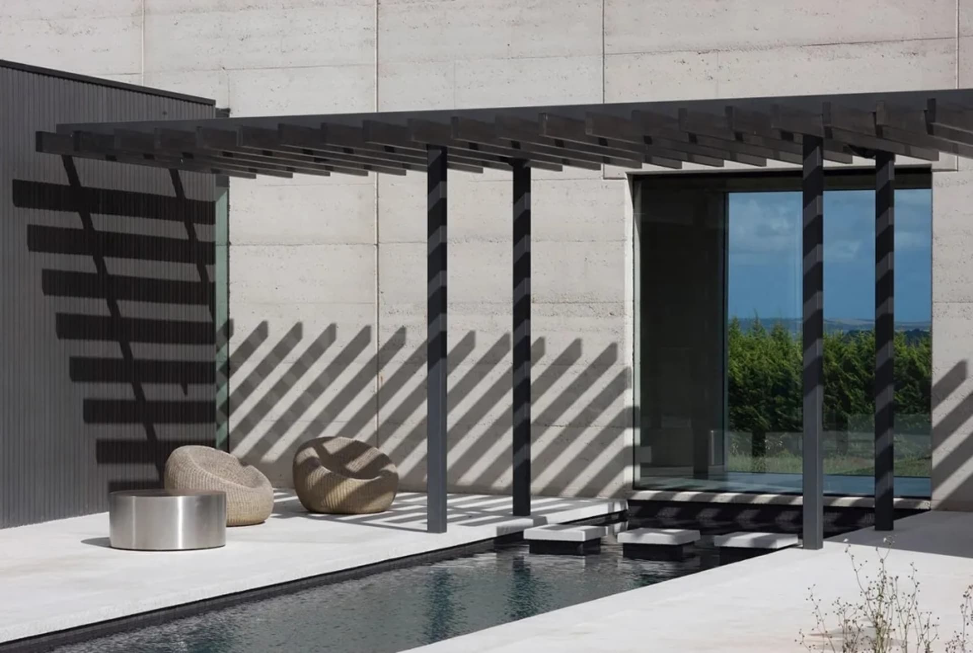 A minimalist residential patio with a concrete floor, a glass-enclosed area, and a pergola structure.