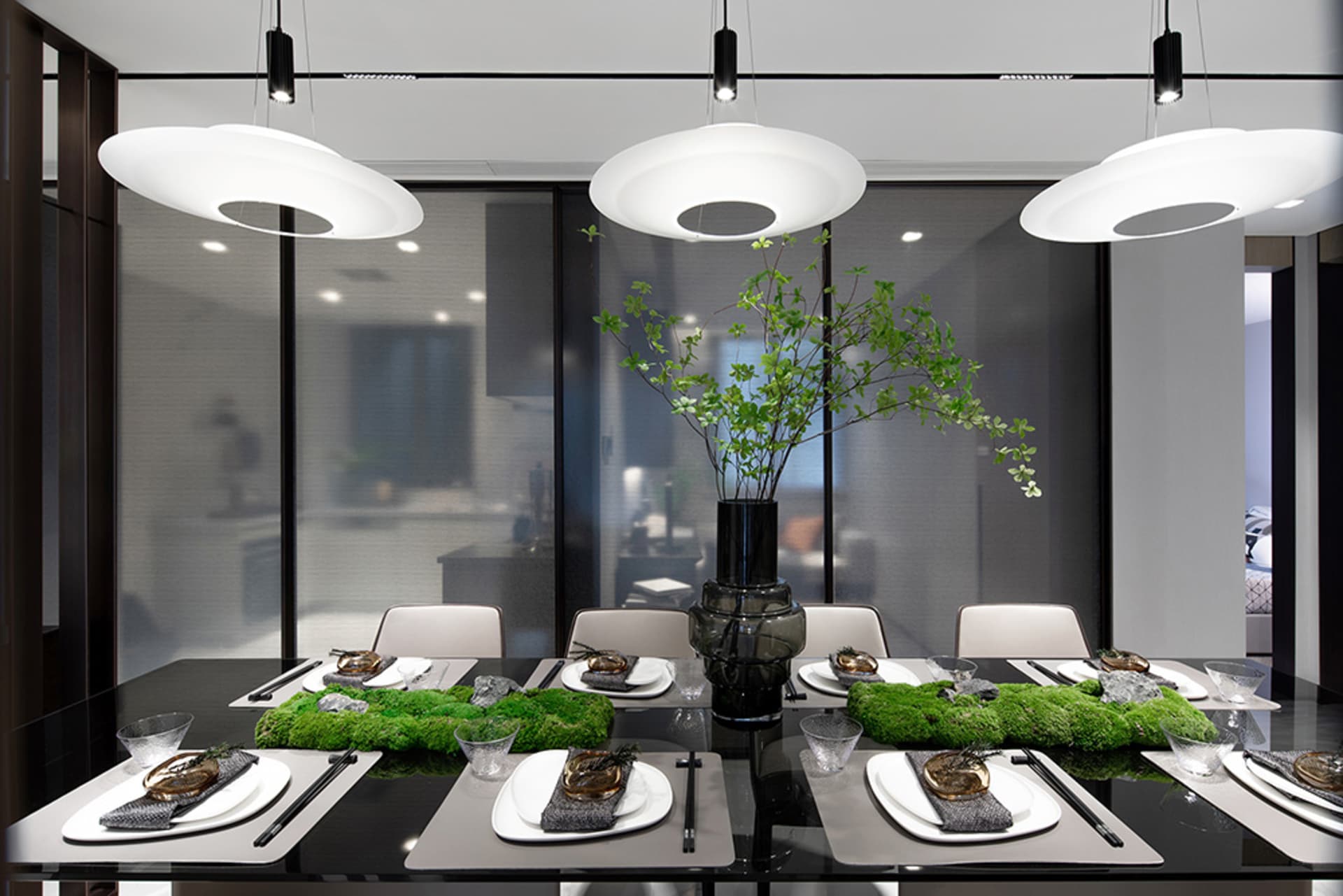 A modern dining room with black glass table, green moss accents, and minimalist decor.