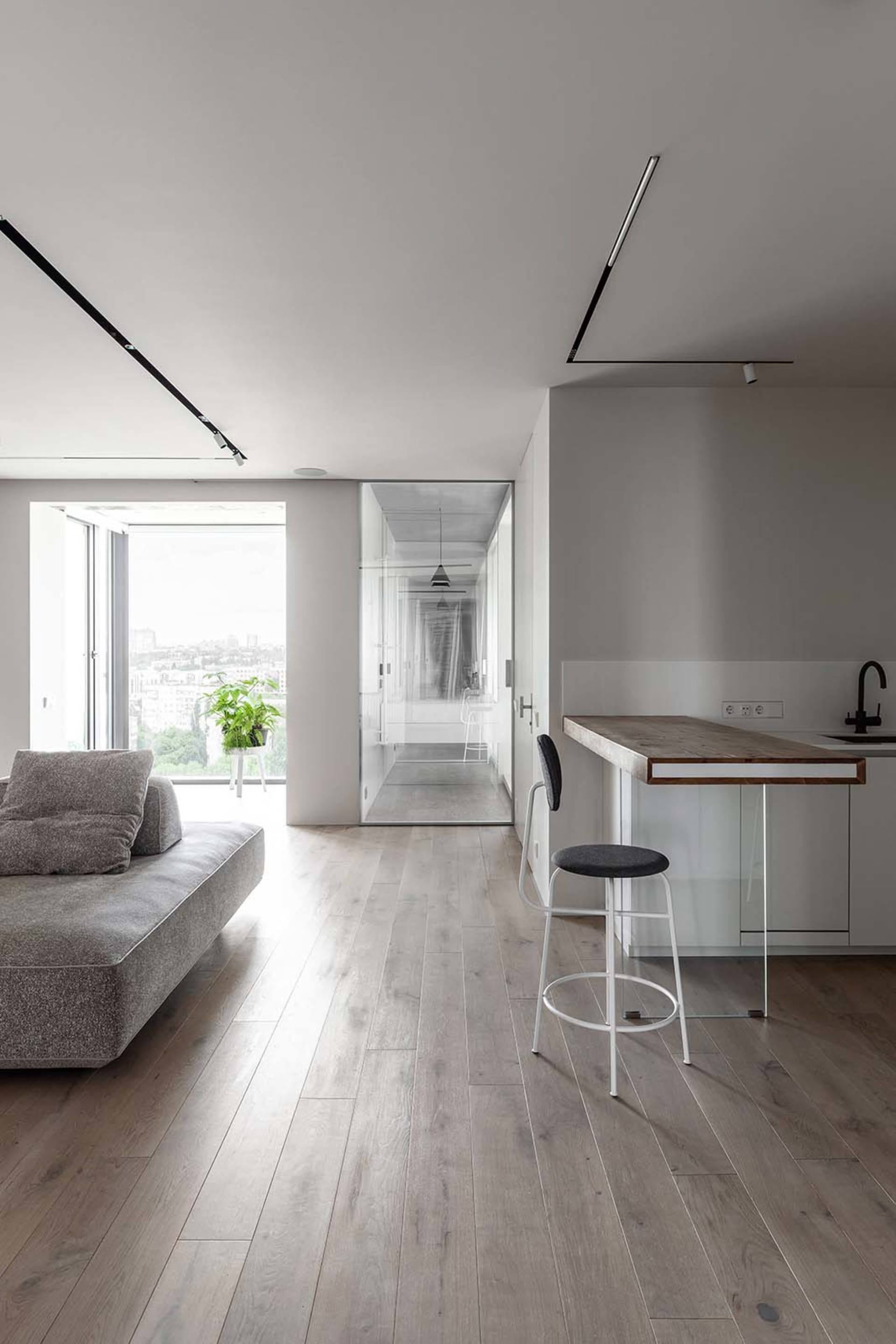 A modern living space featuring wooden flooring, glass partitions, and metallic elements.