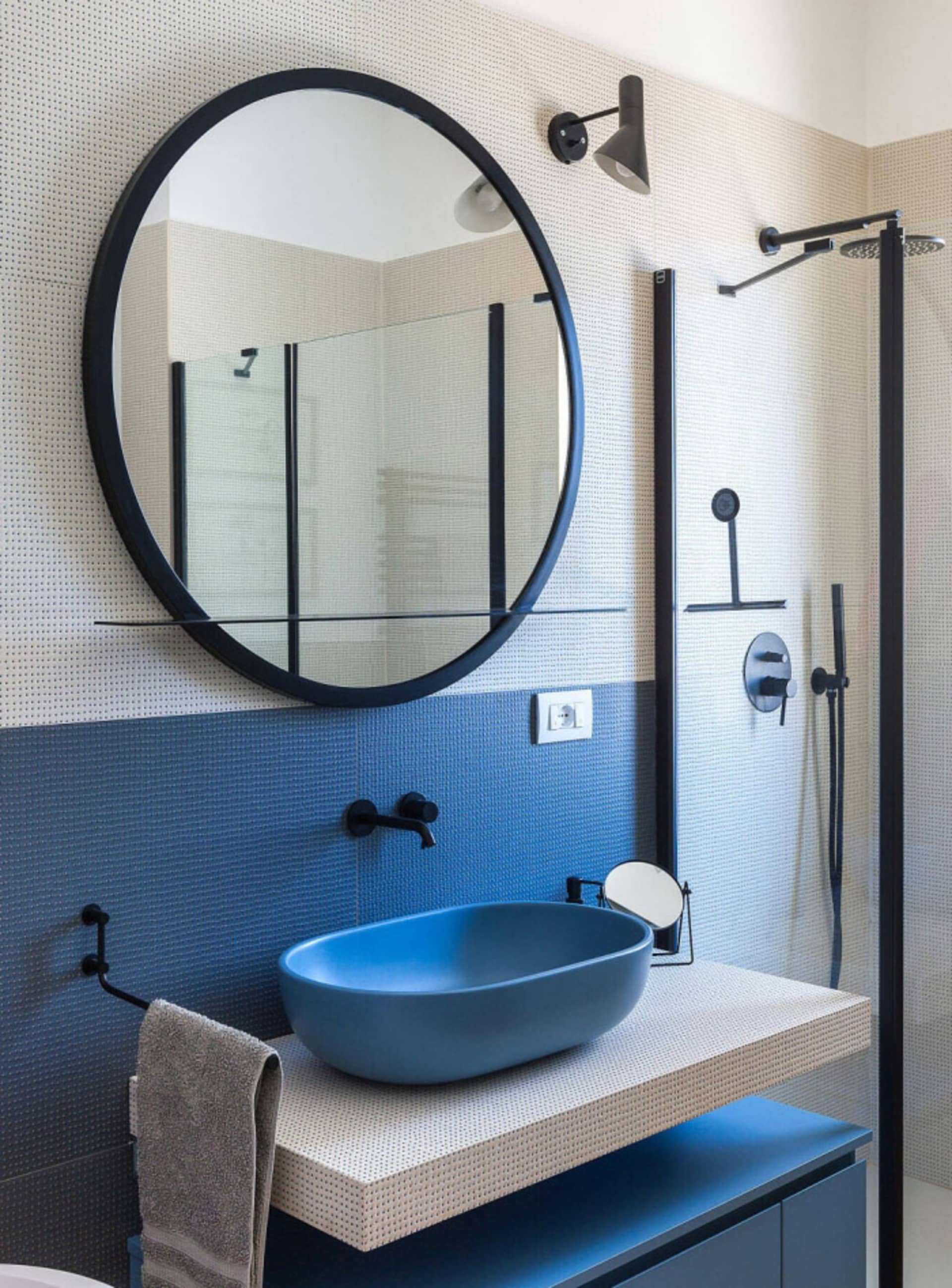 Modern minimalist bathroom with blue tiles, a blue ceramic sink, and a round black-framed mirror.