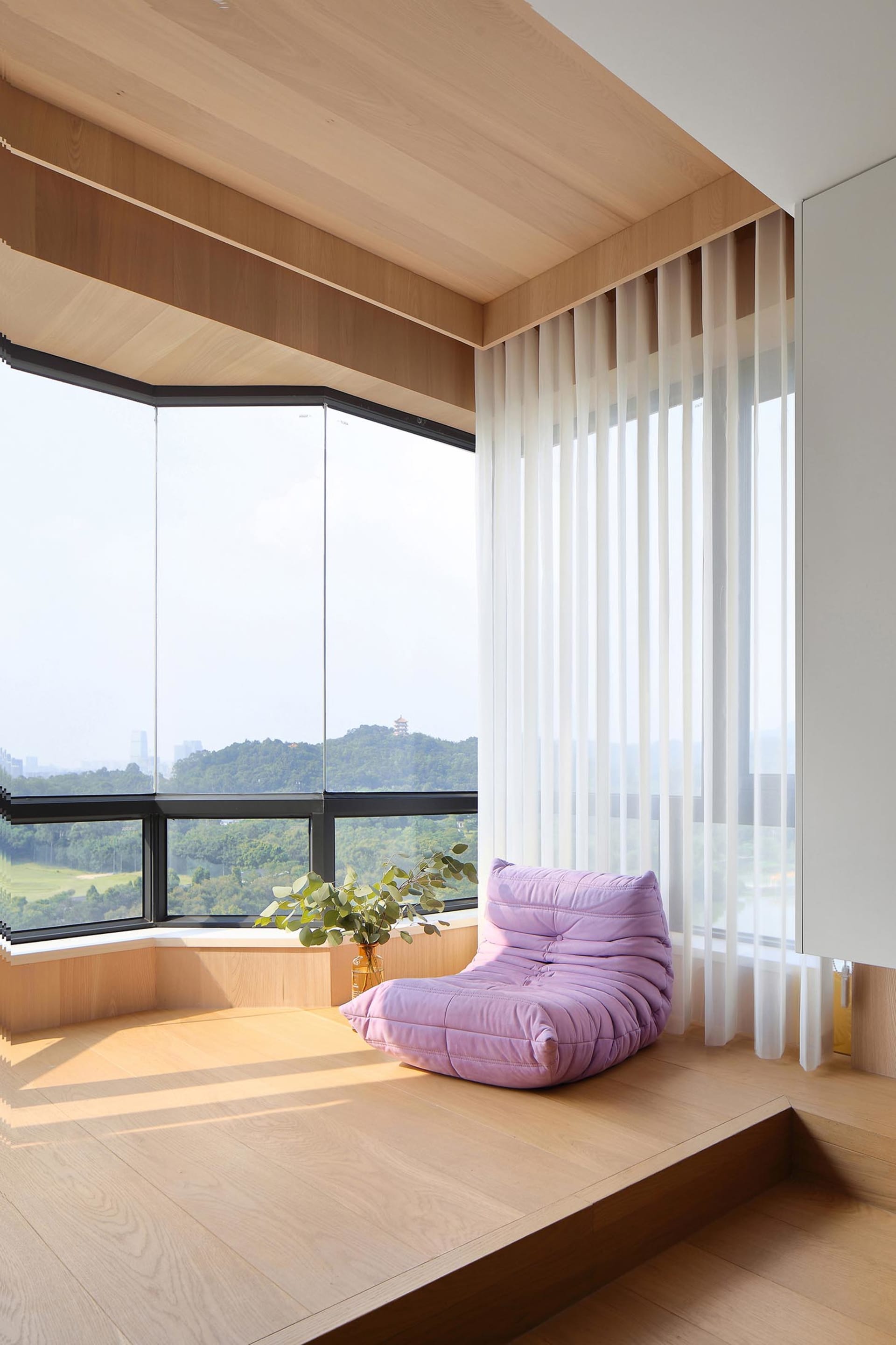 Modern window seat with a purple cushion and green plants, framed by large windows and wooden flooring.