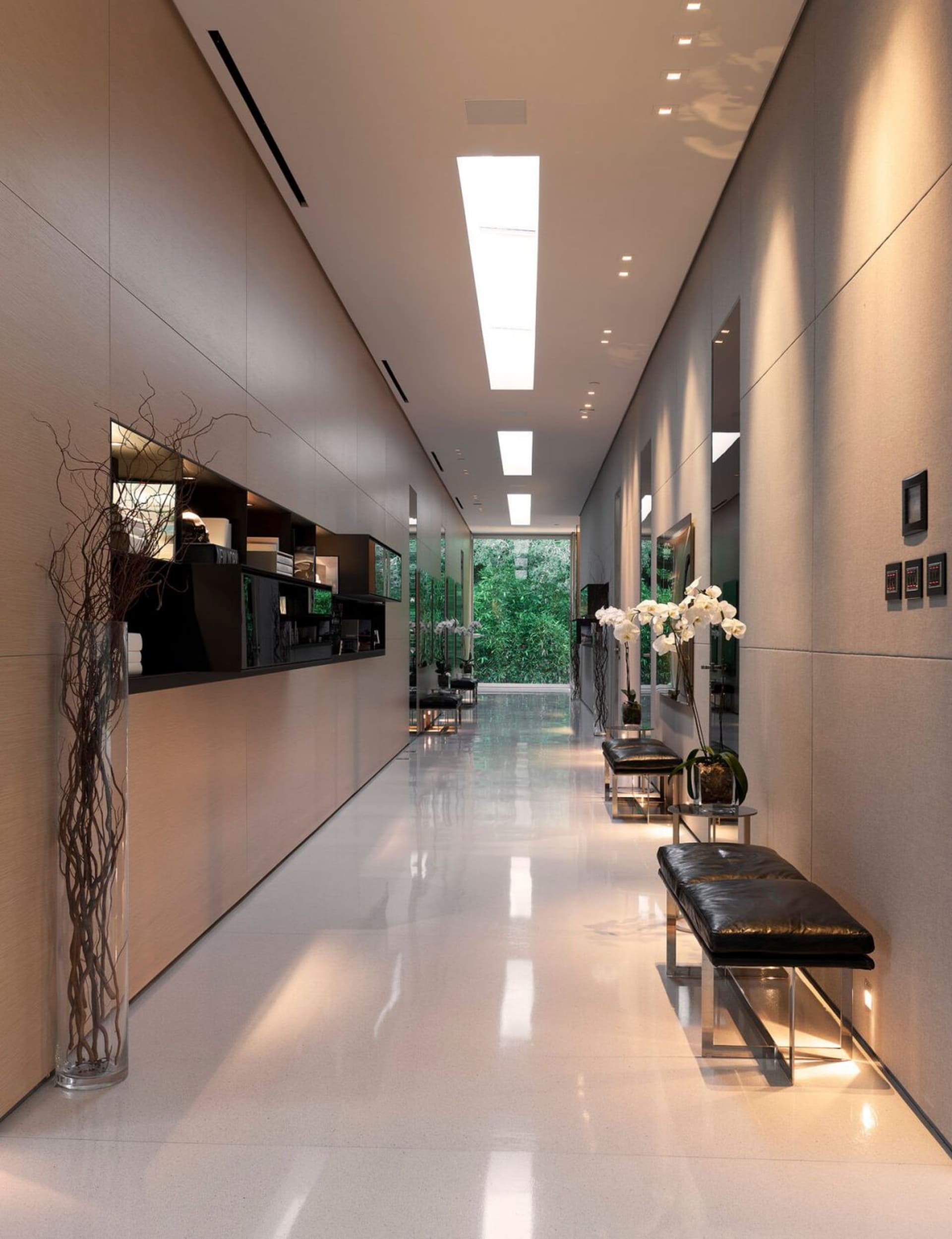 Modern interior design featuring glass and concrete materials in a long corridor with a view of greenery.