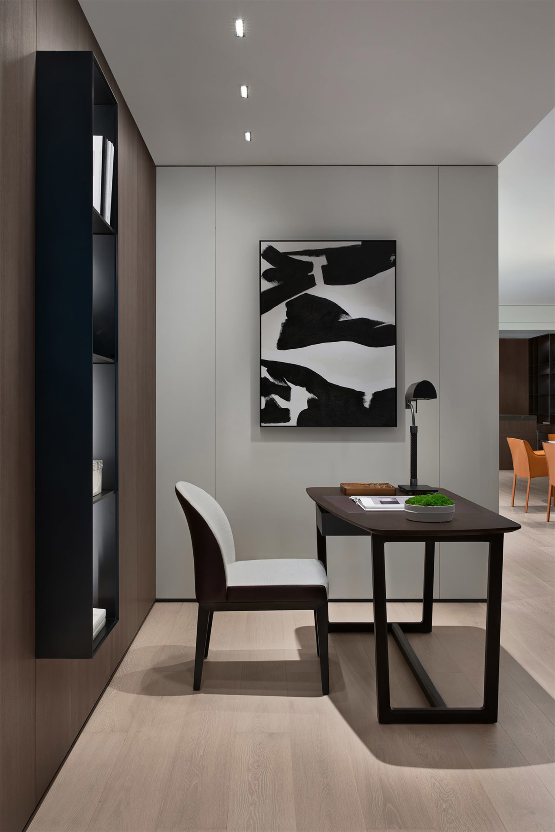 A modern industrial home office with a wooden desk and chair, a black and white abstract painting, and a built-in floating sh