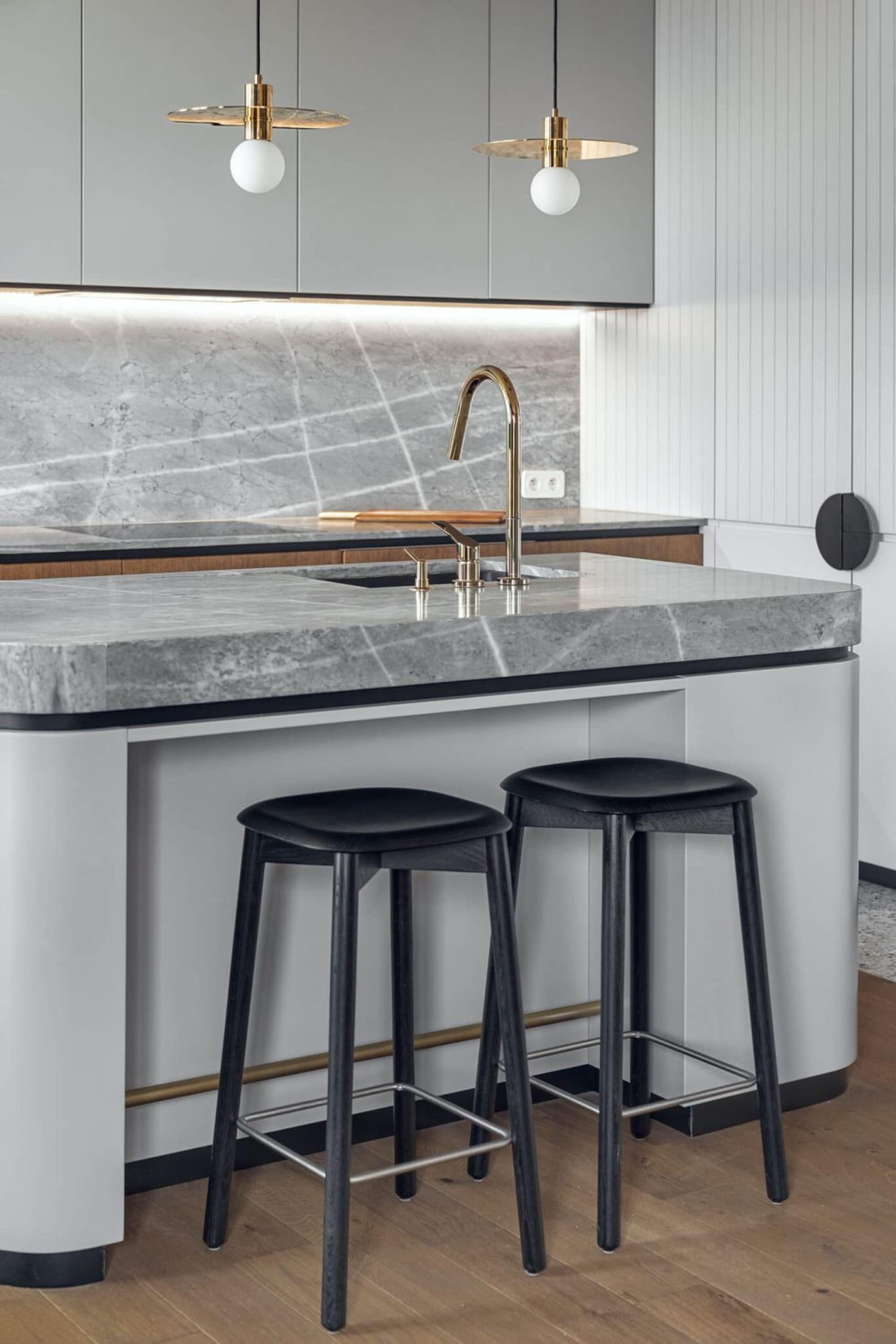 A modern kitchen with a marble countertop, featuring a bar with stools and a sleek faucet with a brass finish.