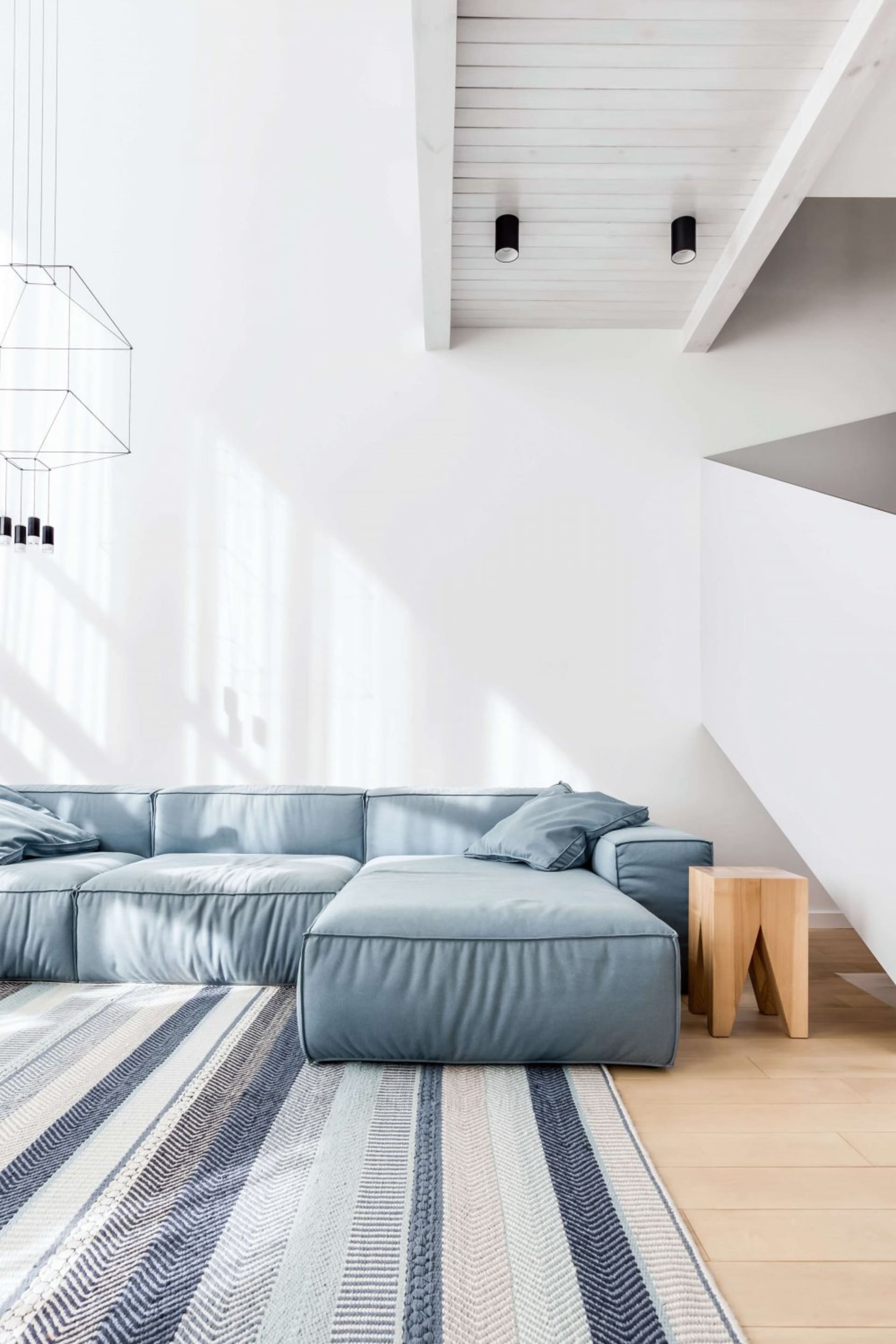 A modern minimalist living room featuring a fabric sofa, wooden stool, and a striped rug.