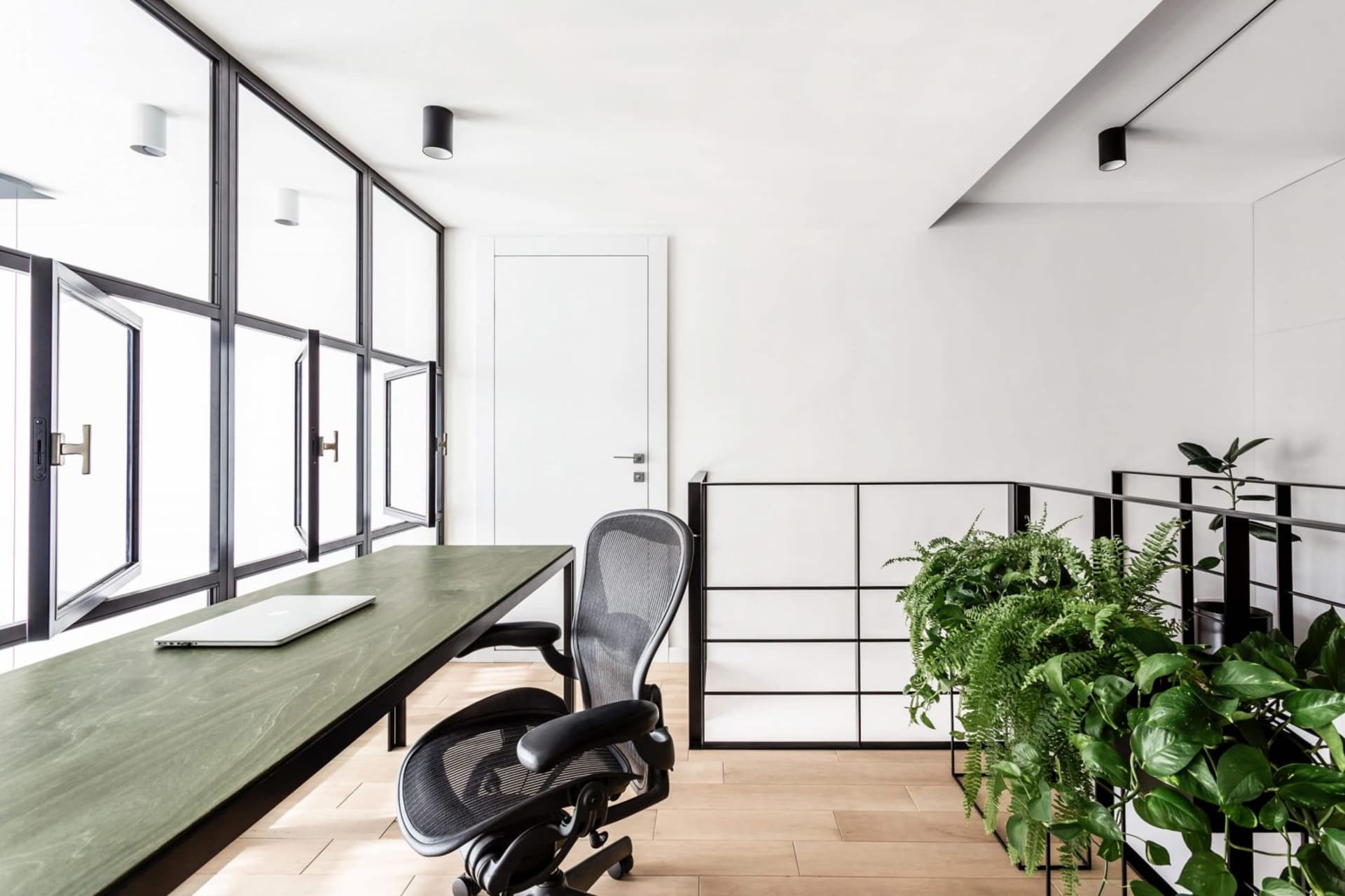 Modern office with metal-framed glass walls, green desk, and wooden flooring