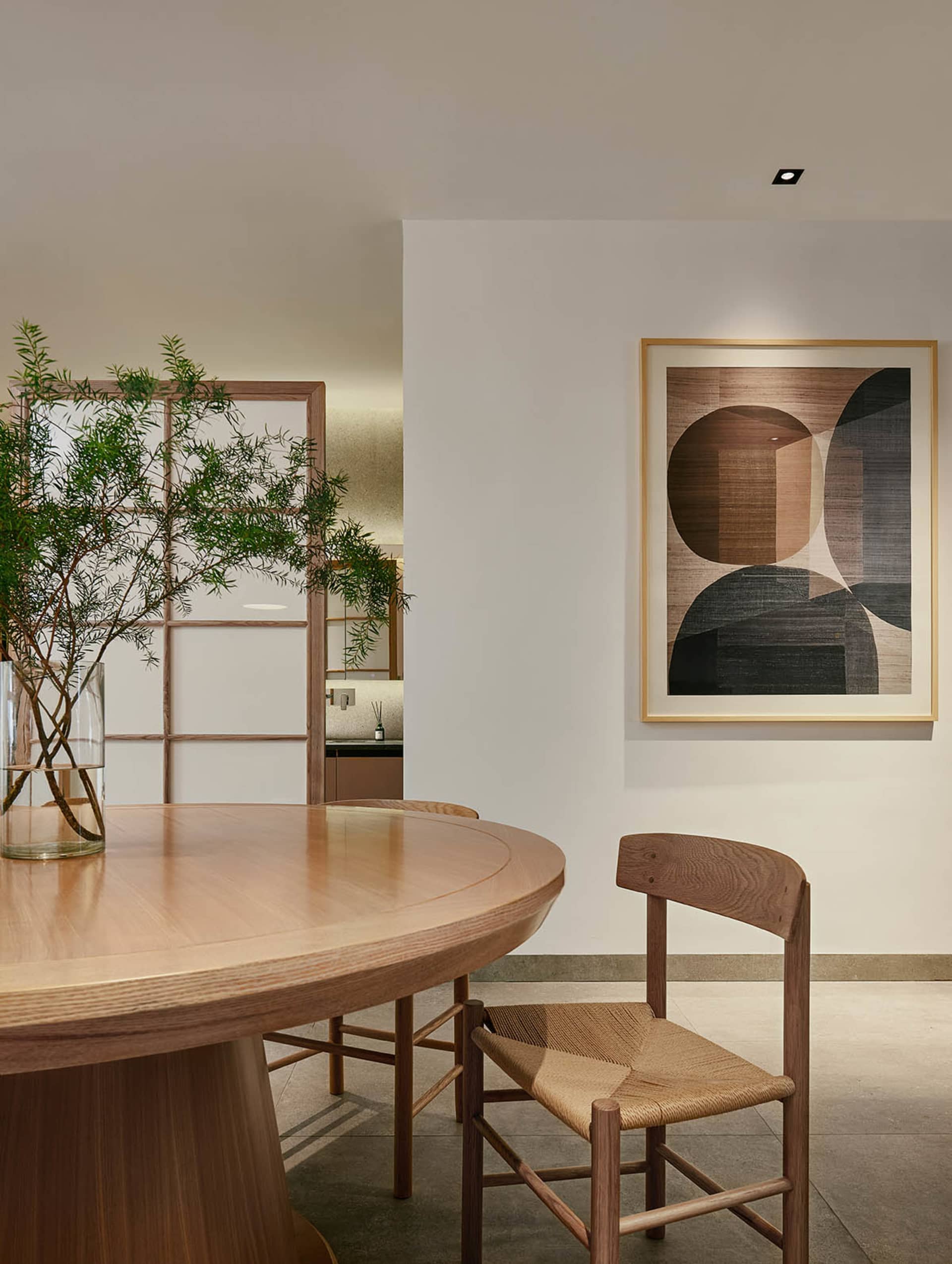 A modern dining room with a wooden table, chairs, and a plant in a vase.
