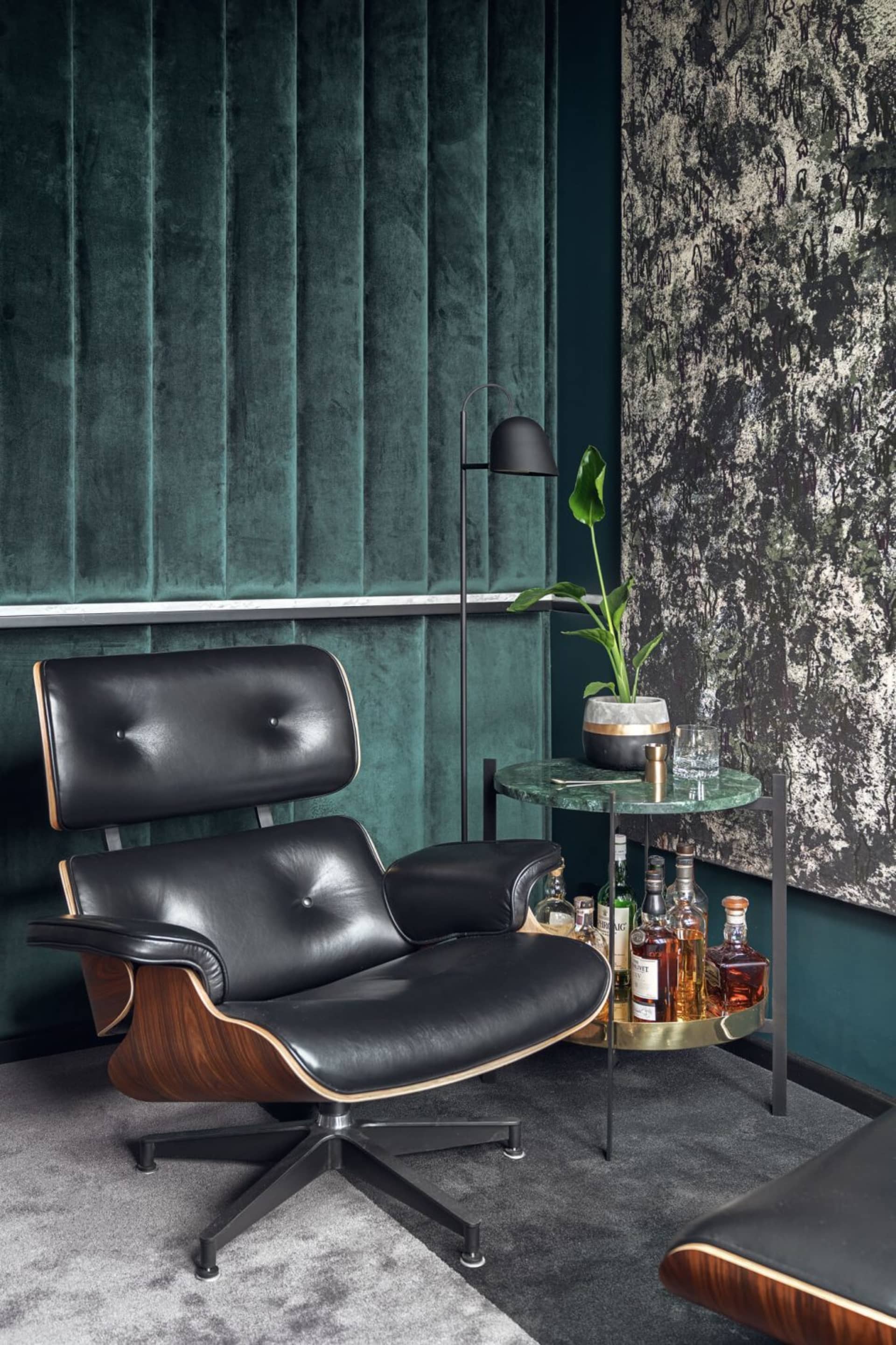 Modern living room featuring a black leather armchair with wooden accents and a side table with drinks and plants.