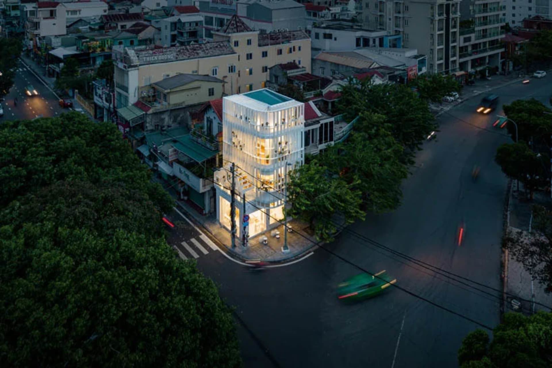 黃昏時分的現代玻璃建築外觀，窗戶燈光亮起，街道上停著一輛綠色汽車。