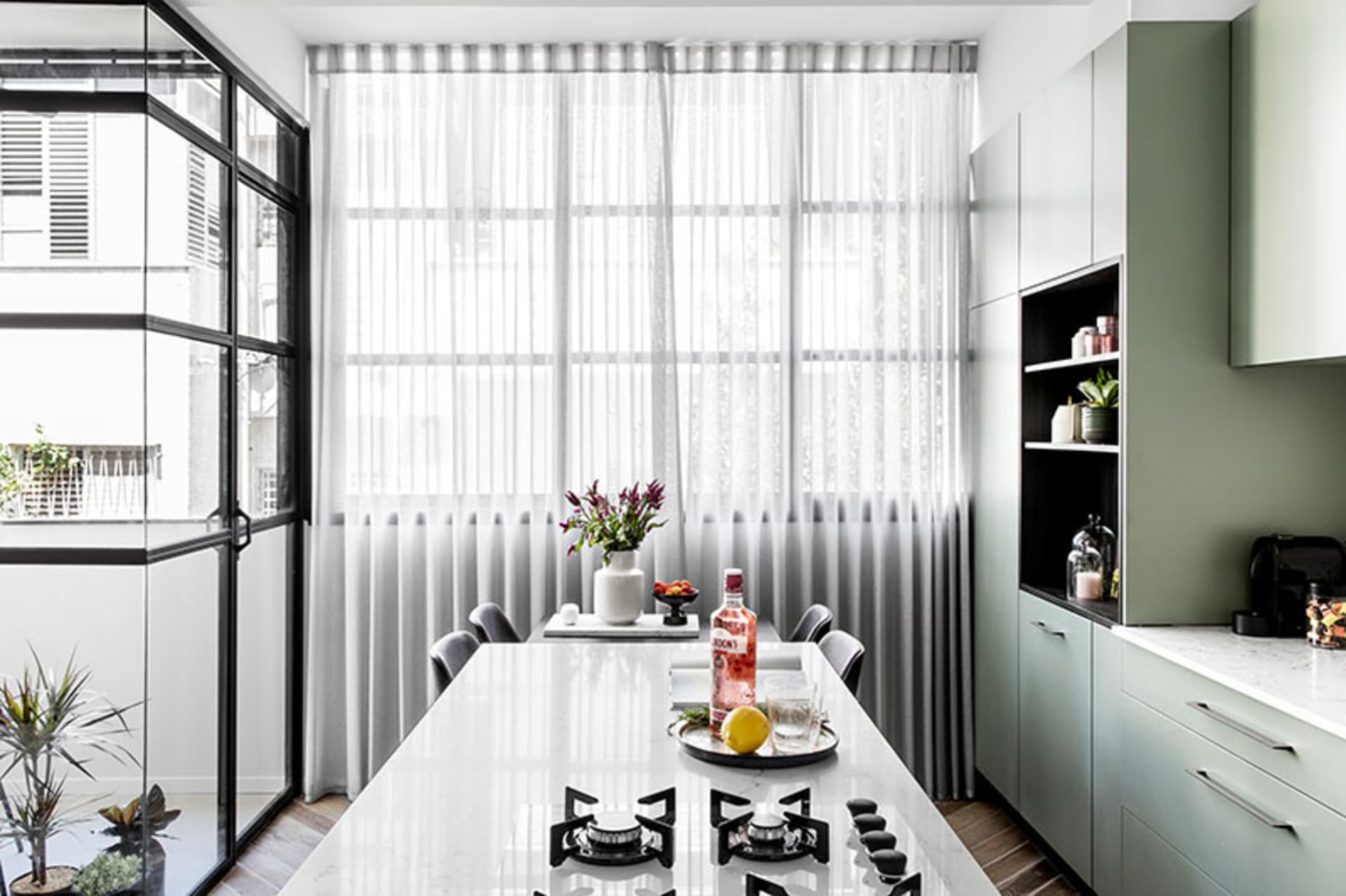 A contemporary kitchen with marble countertops, green cabinets, glass windows, and canvas wall art.