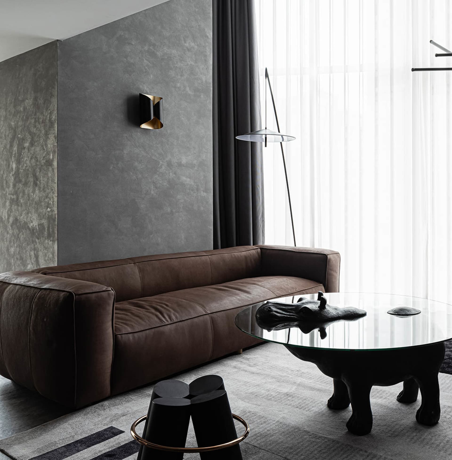 A modern living room featuring a brown leather couch and a glass table with a hippo sculpture.