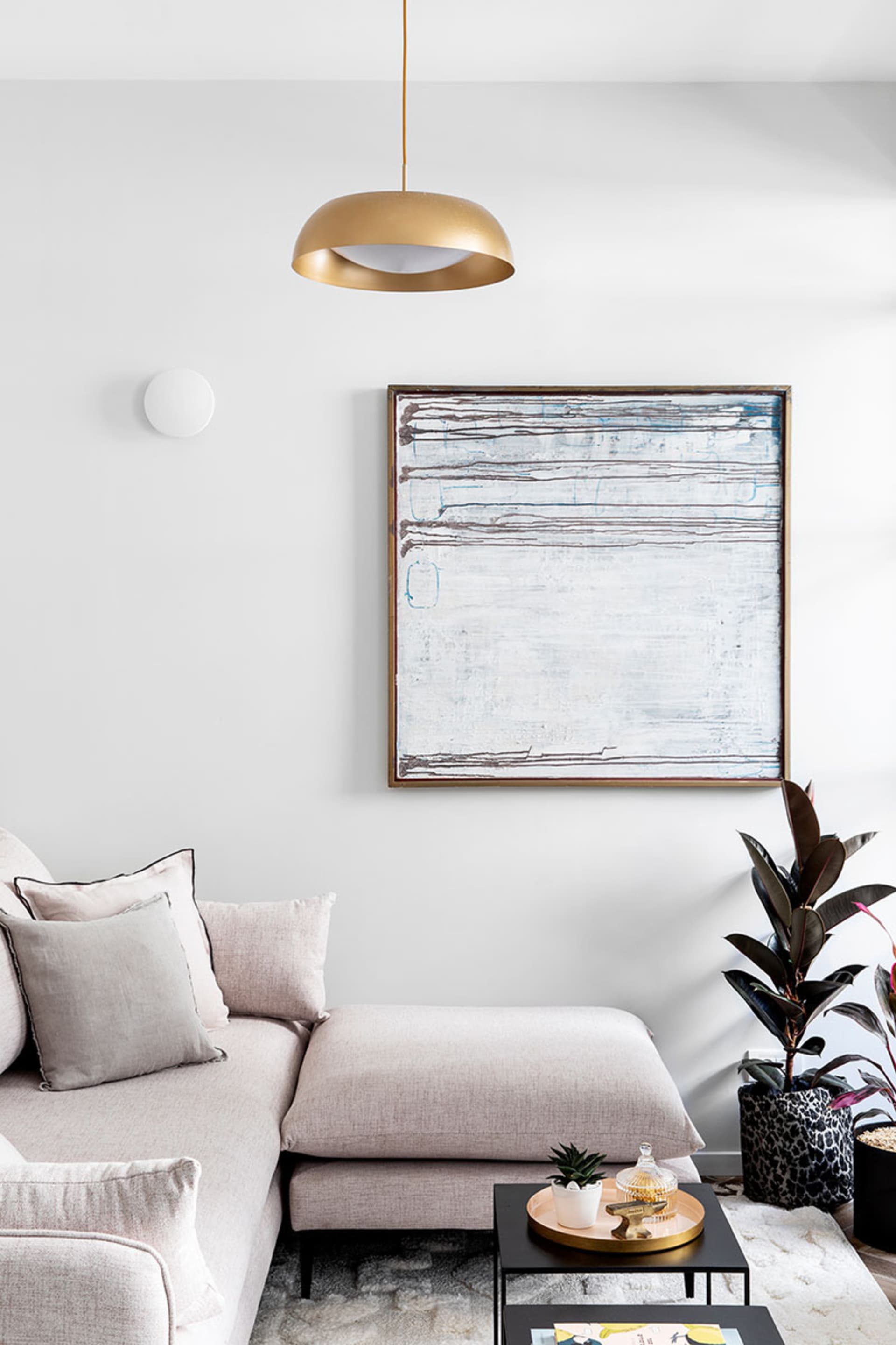 A modern living room with a beige sofa, pendant light, abstract art, and a small coffee table with a plant and candle.