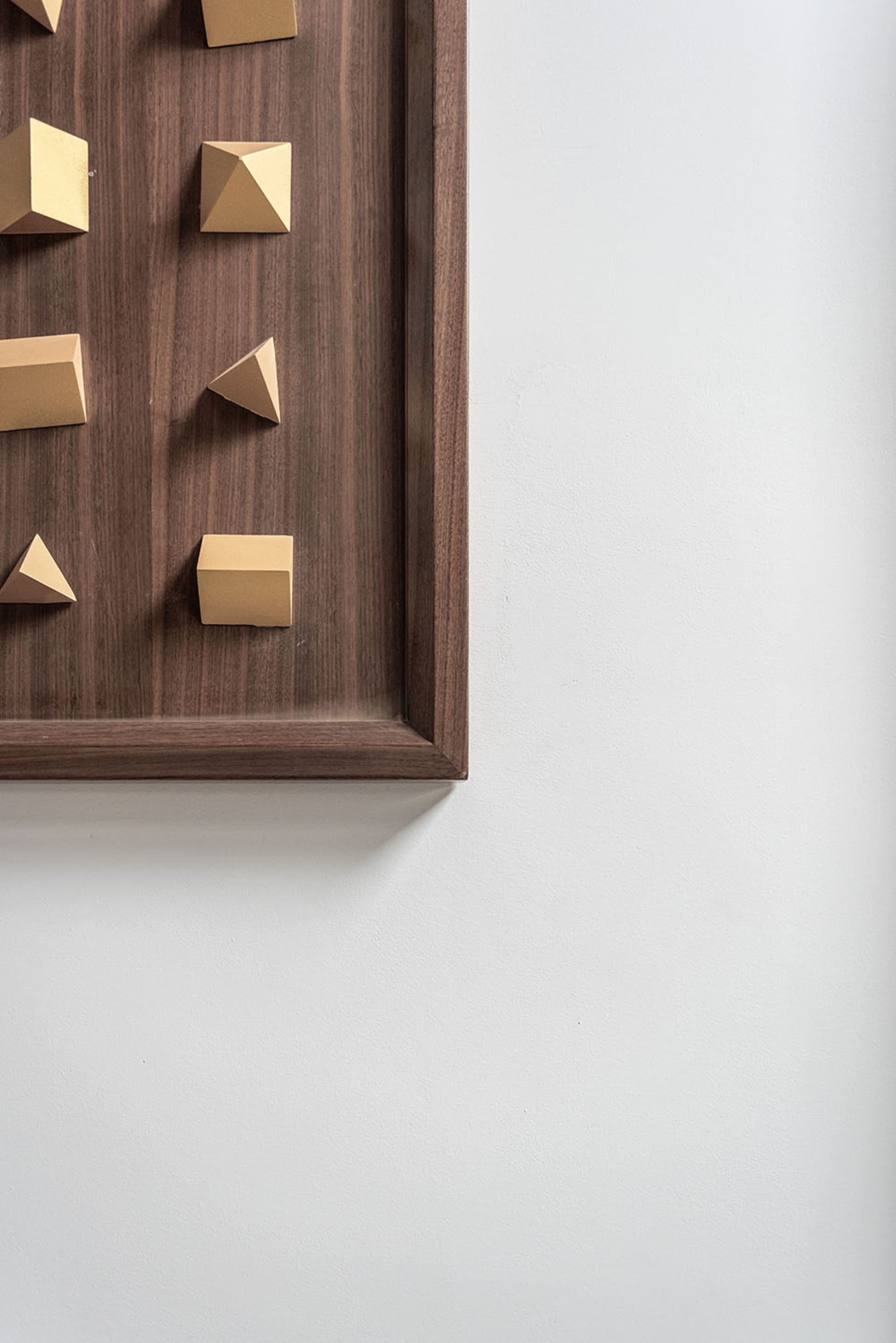 Gold-colored geometric shapes mounted on a wooden frame hanging on a white wall.