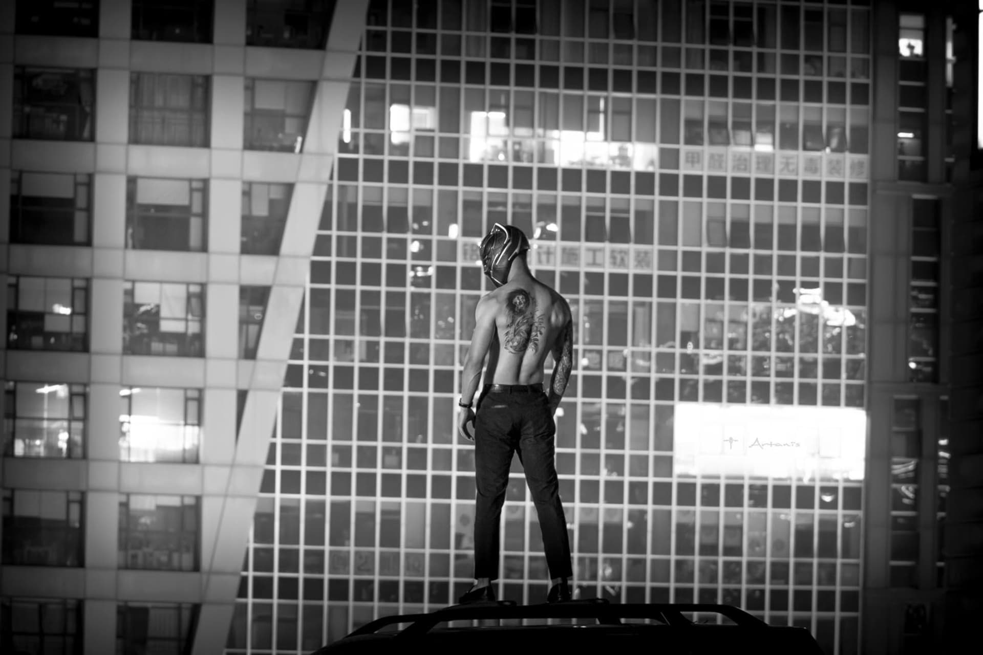 A shirtless man standing on a concrete rooftop with a cityscape background.