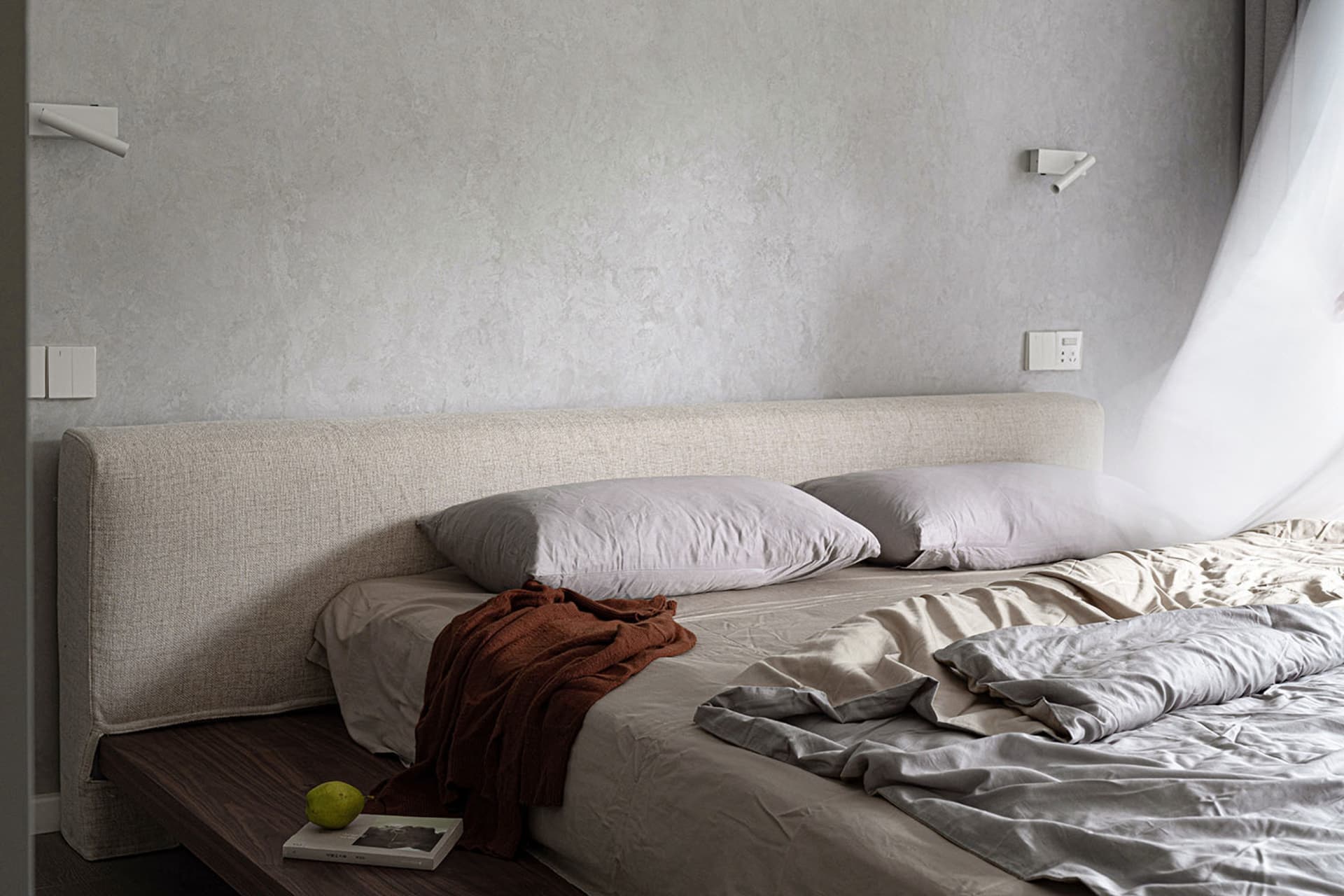 Modern minimalist bedroom featuring a textured fabric headboard and linen bedding.