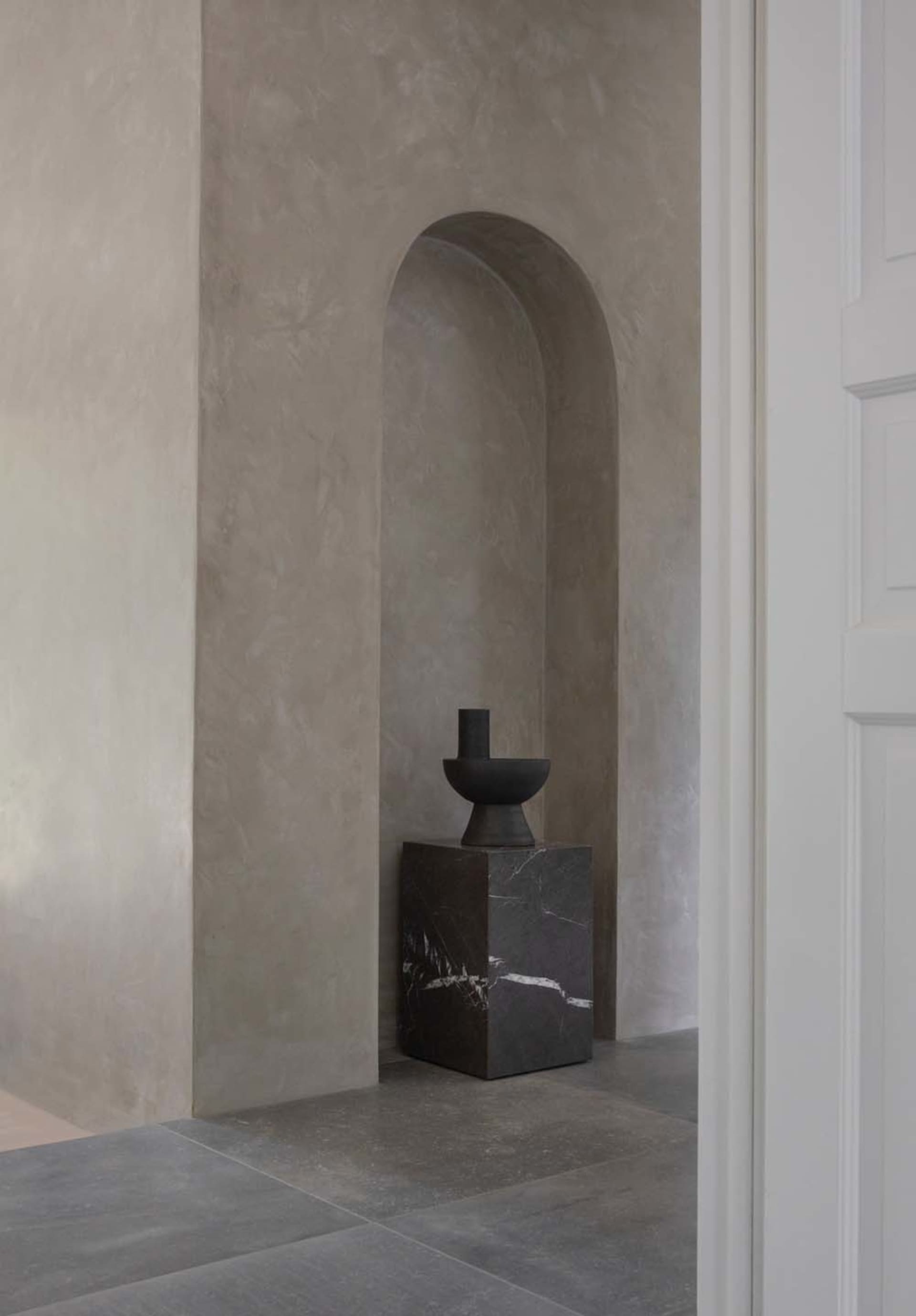 A modern minimalist living room featuring a single piece of furniture made from dark concrete, positioned against a plain con