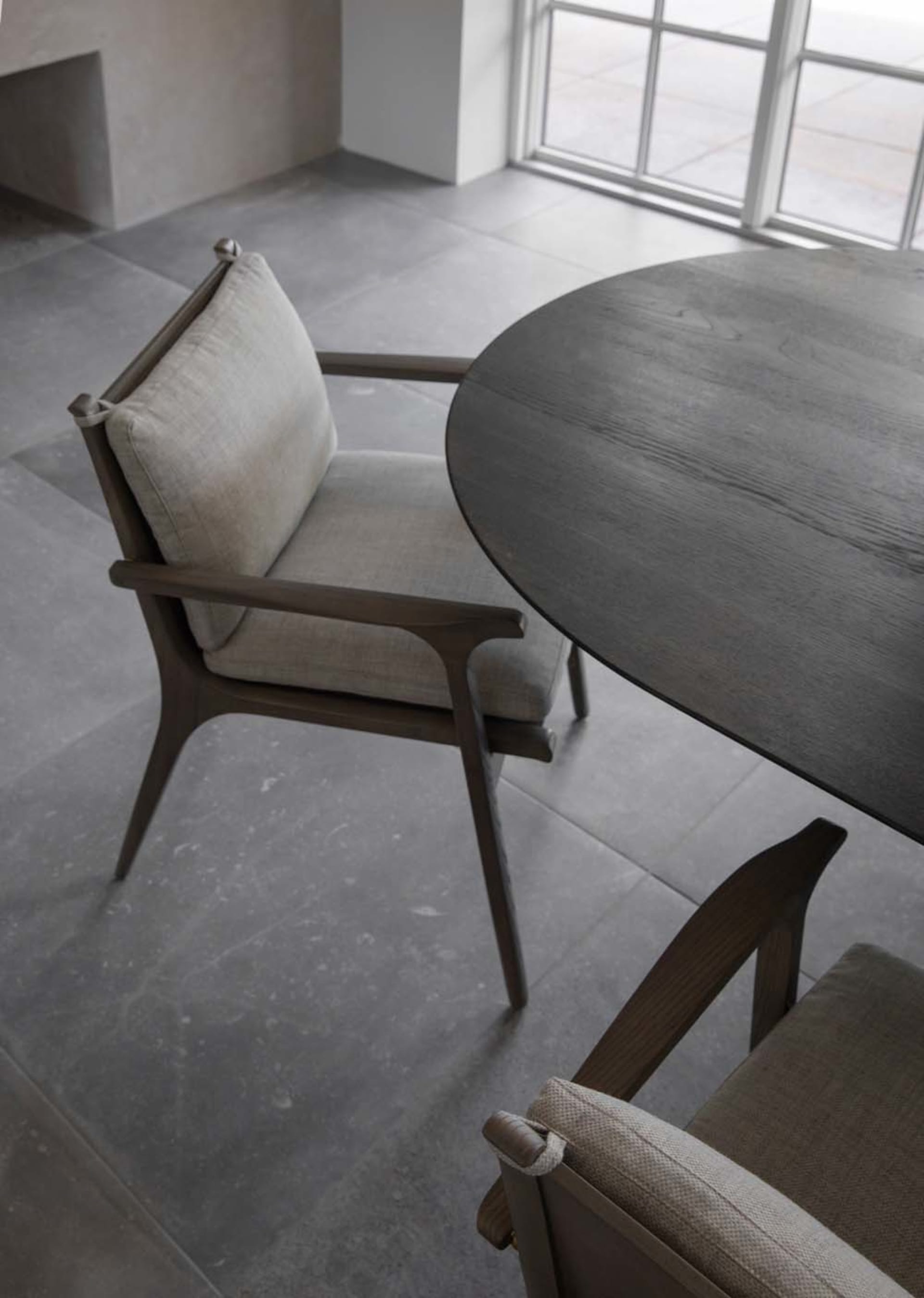 Modern dining room with a round wooden table and upholstered chairs with light-colored cushions.