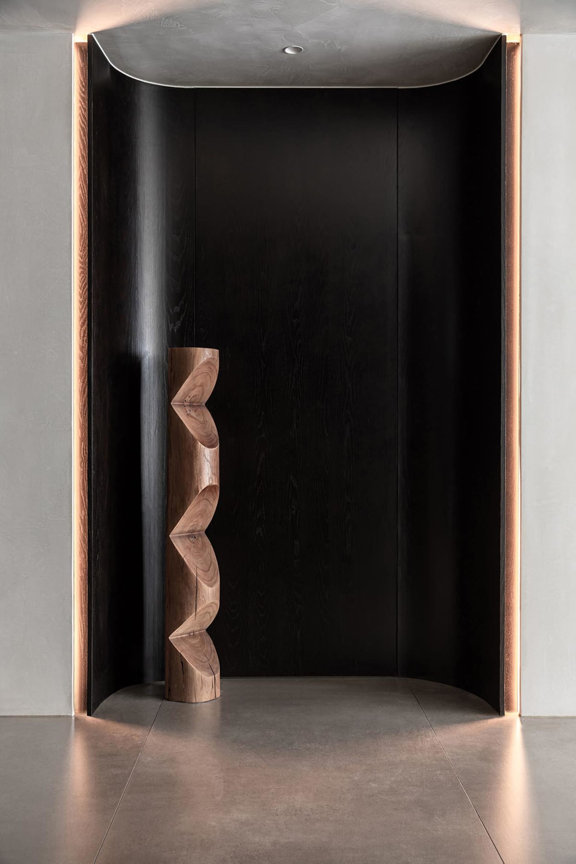 A modern entryway featuring black wooden panels and a sculptural wooden piece with wave-like patterns.