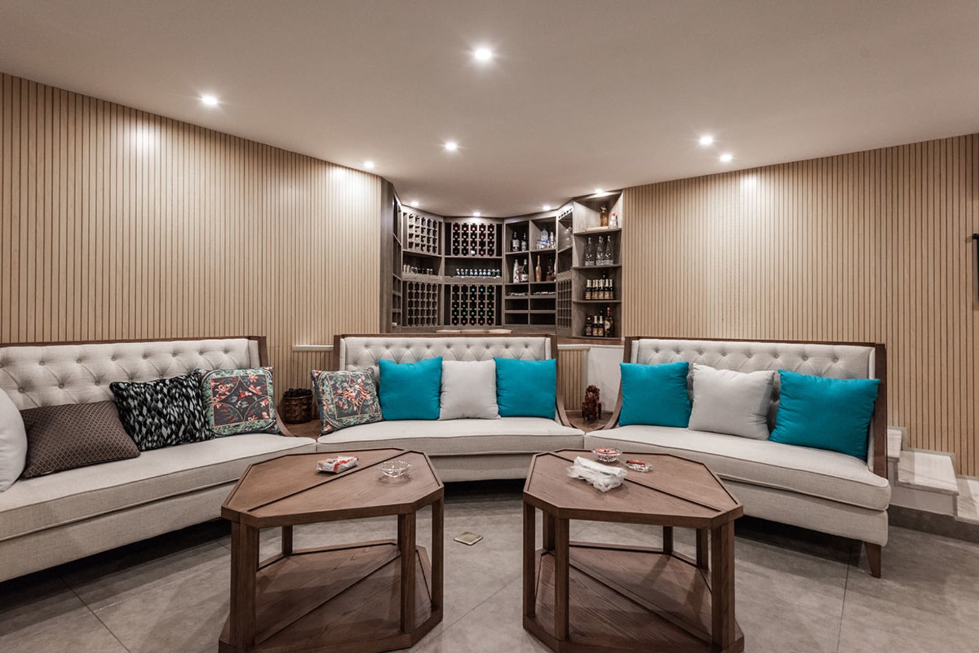 Modern living room featuring white sofas with blue and white cushions, wooden walls, and glass coffee tables.