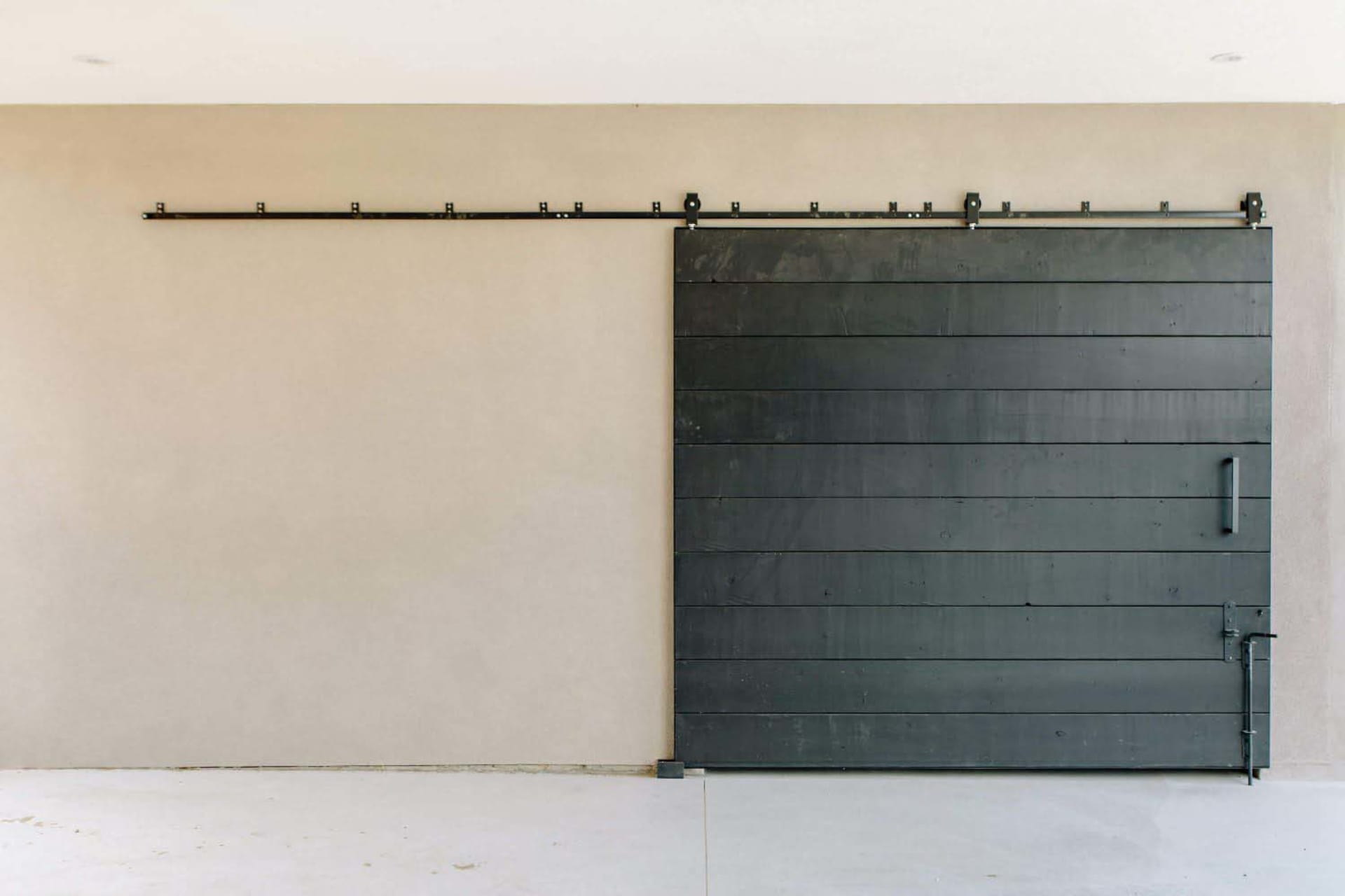 A modern, minimalist barn door wall featuring a horizontal black slat wall on a beige wall with a black metal rail mounted ab