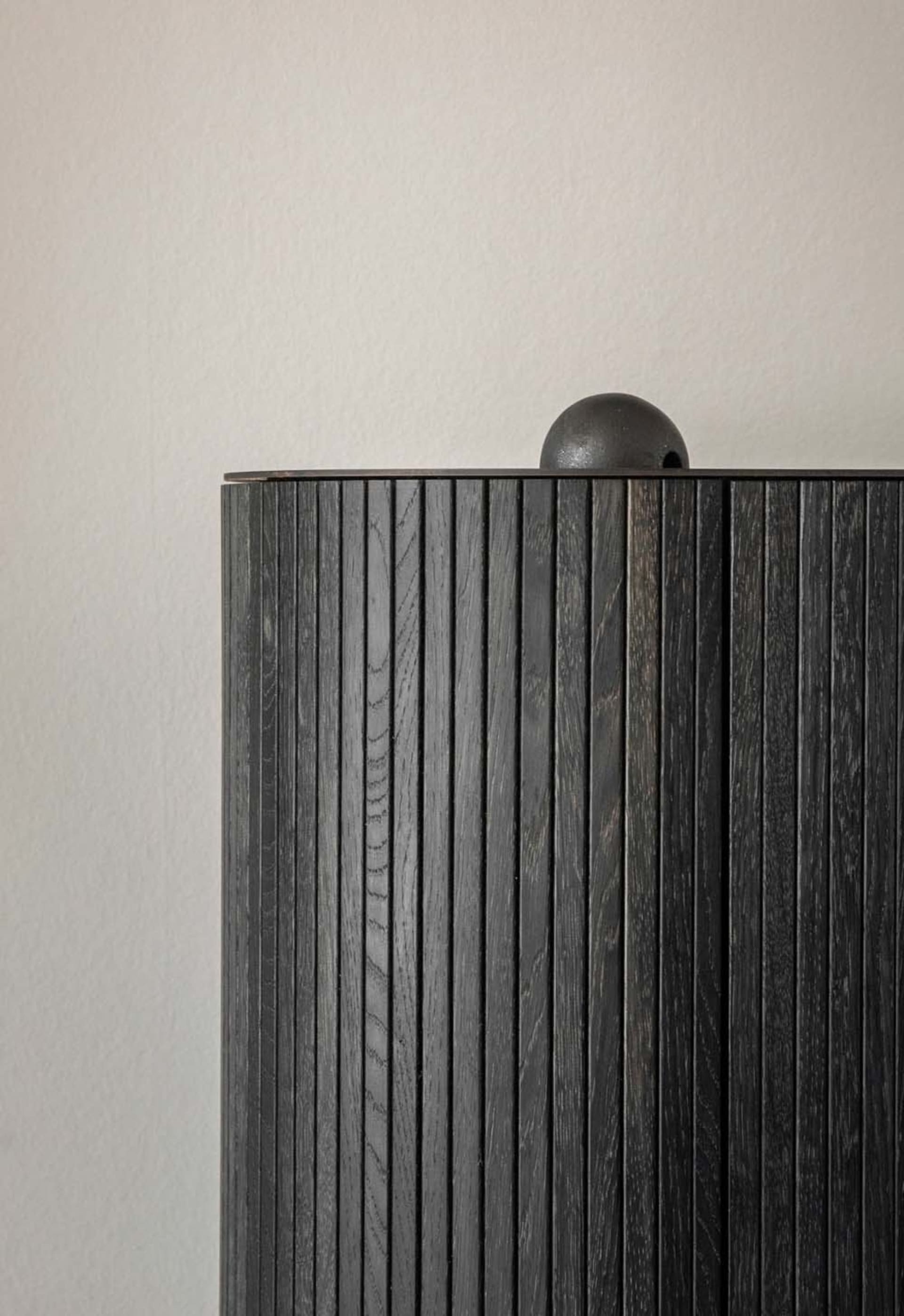 A photograph of a modern, dark wood wardrobe with vertical slats and a round top.