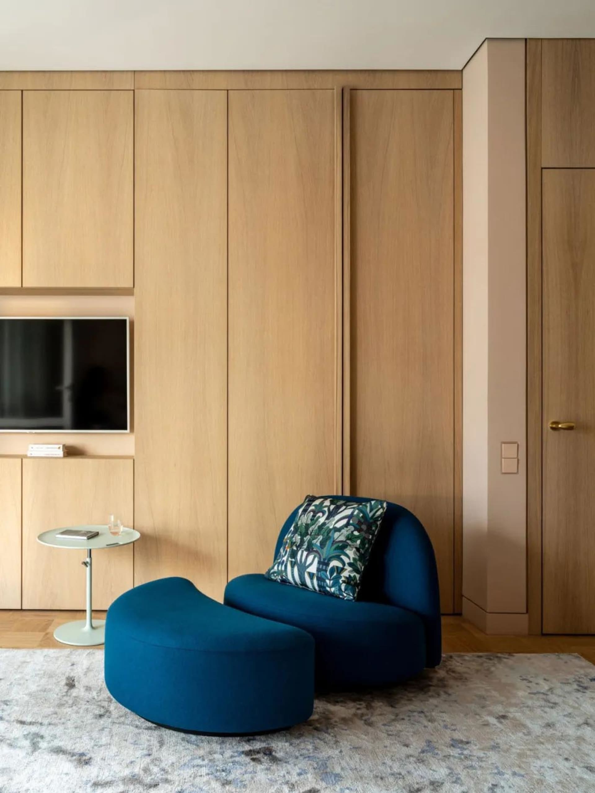 Modern living room with wooden cabinets, a blue sofa, and a patterned rug.