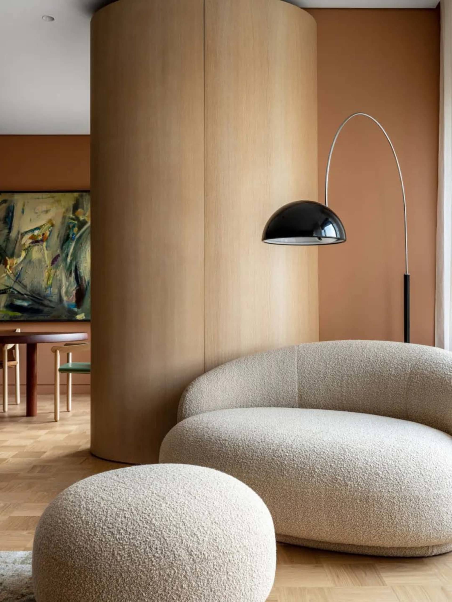 Modern minimalist living room with a circular sofa, ottoman, and abstract painting.