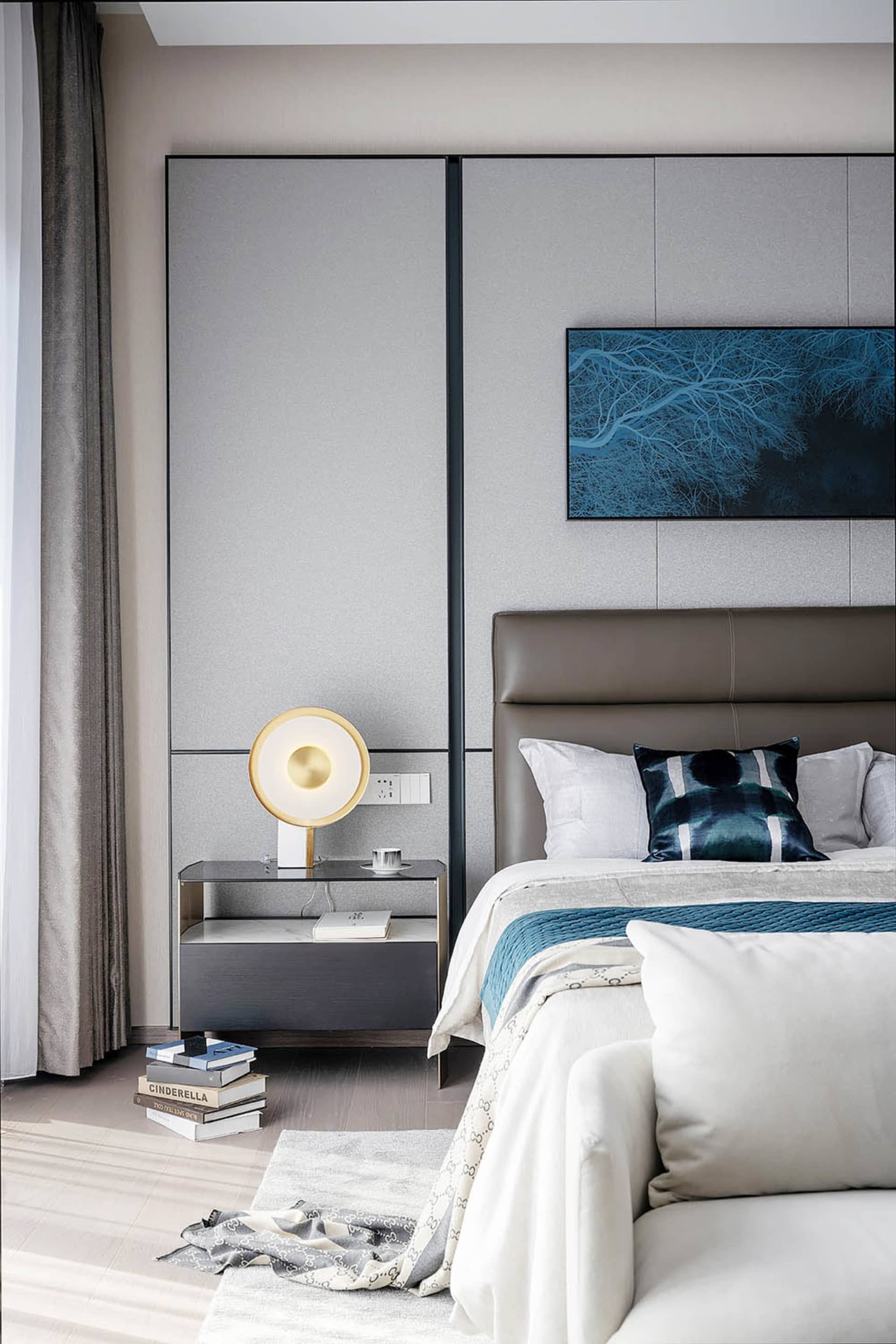 A modern bedroom featuring grey furnishings, a leather headboard, and a glass bedside table.