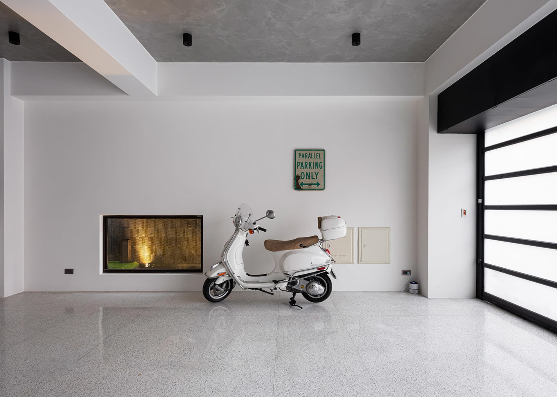 Modern industrial garage interior with minimalist design, featuring concrete flooring and a white Vespa scooter.