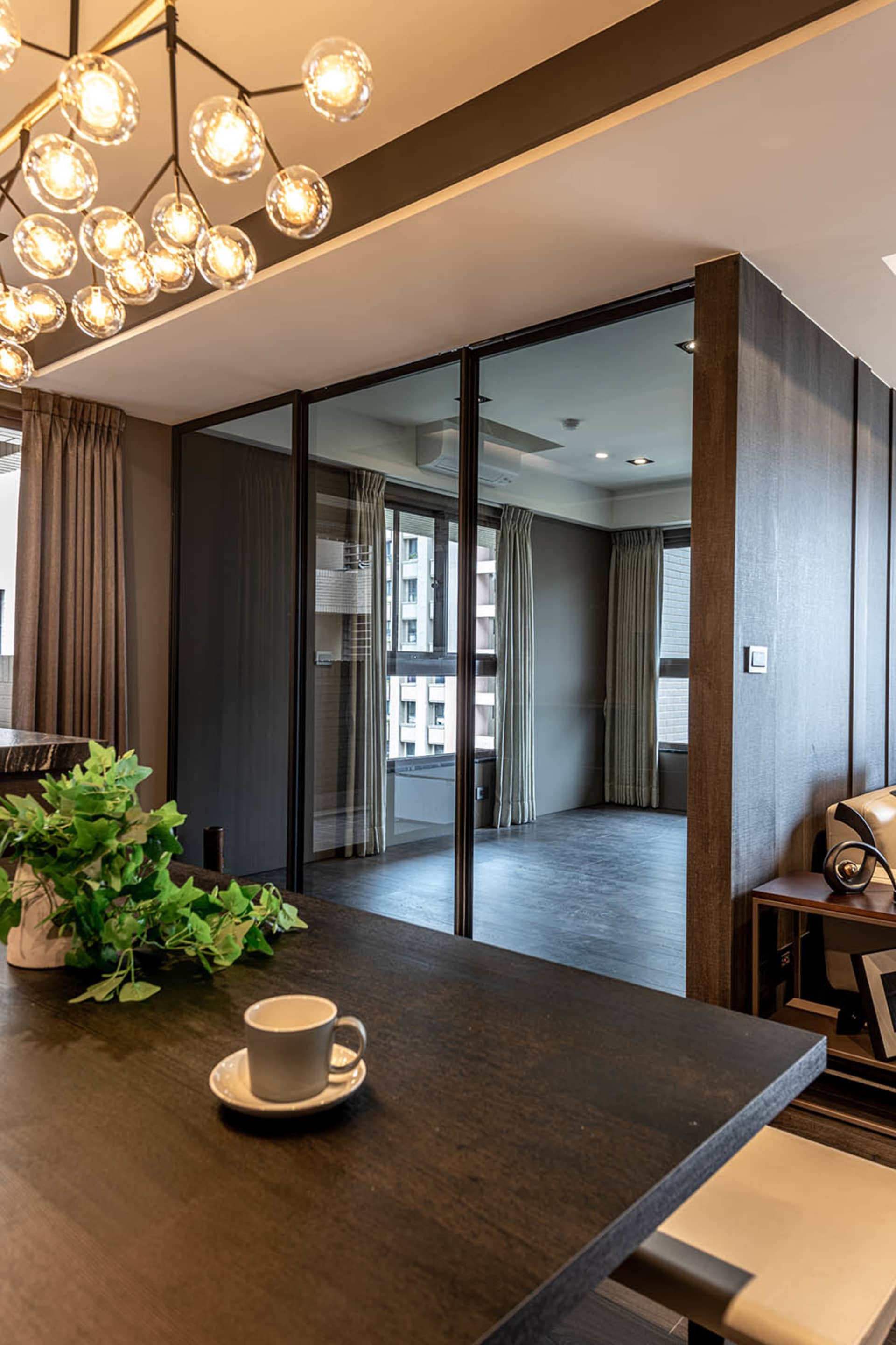 A modern minimalist living room with glass walls, wooden flooring, and fabric furnishings.