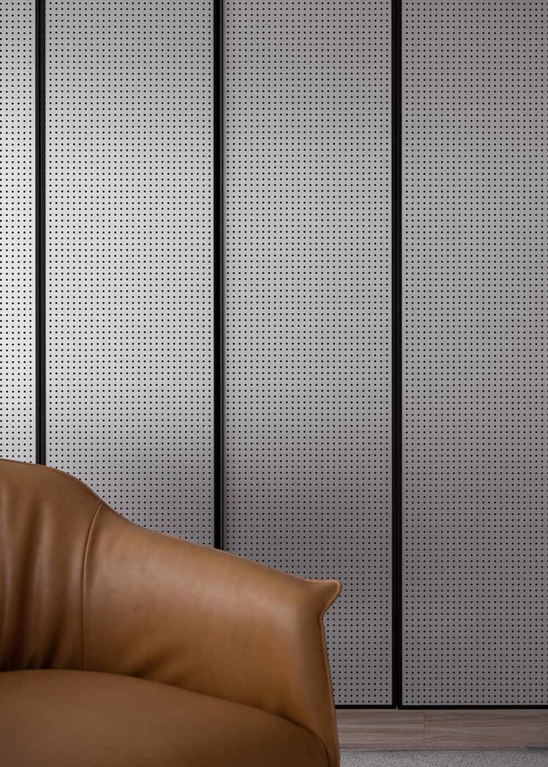 A modern sofa made of brown leather against a perforated metal wall in an industrial setting.