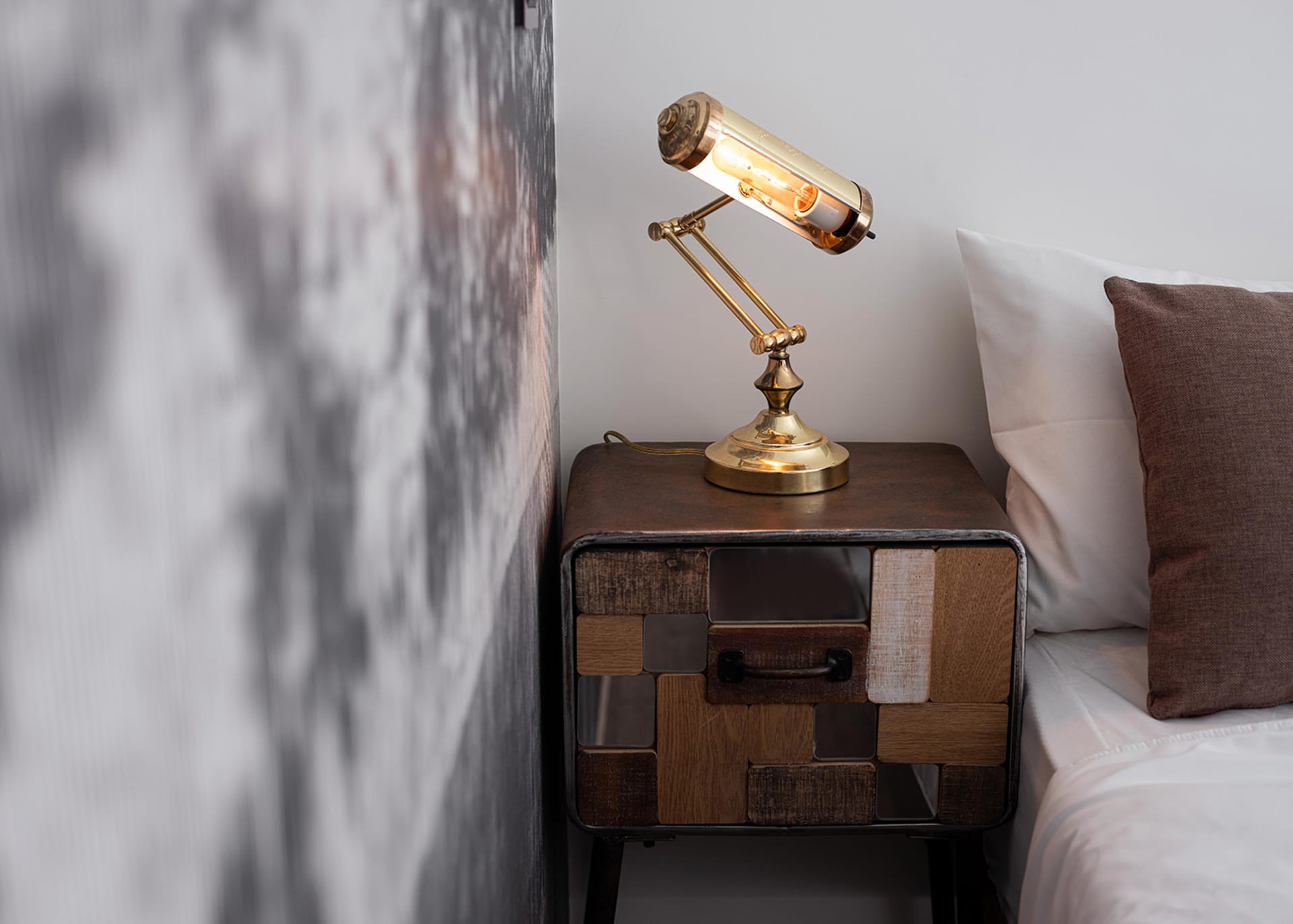 A stylish, industrial-style bedside table made of metal and wood, featuring a unique task light with an exposed bulb.