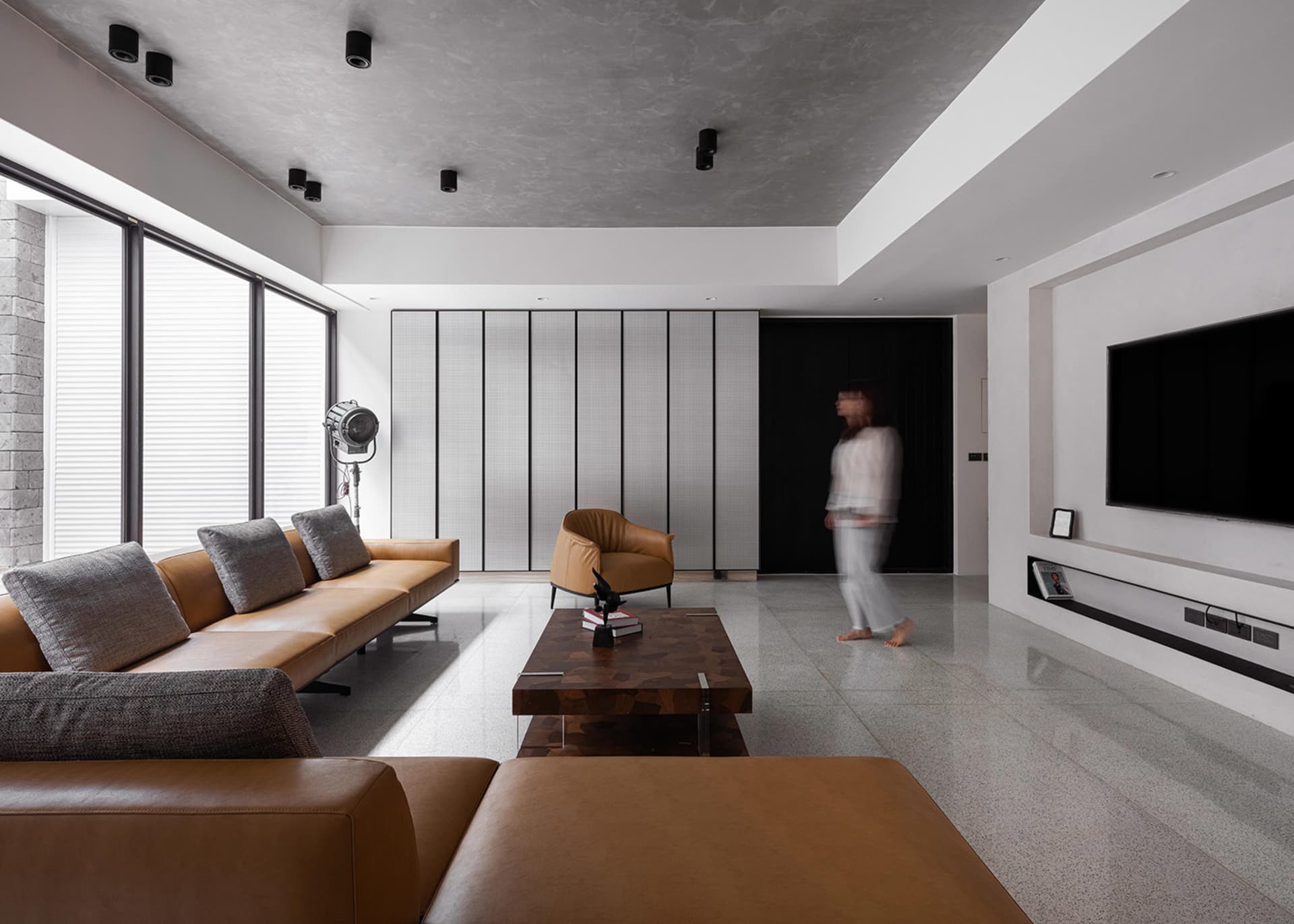 A modern living room with a minimalist design featuring a concrete wall and dark wooden flooring.