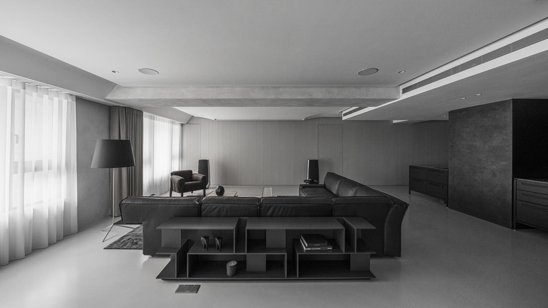 A minimalist living room with black furniture, concrete walls, and a large floor lamp.