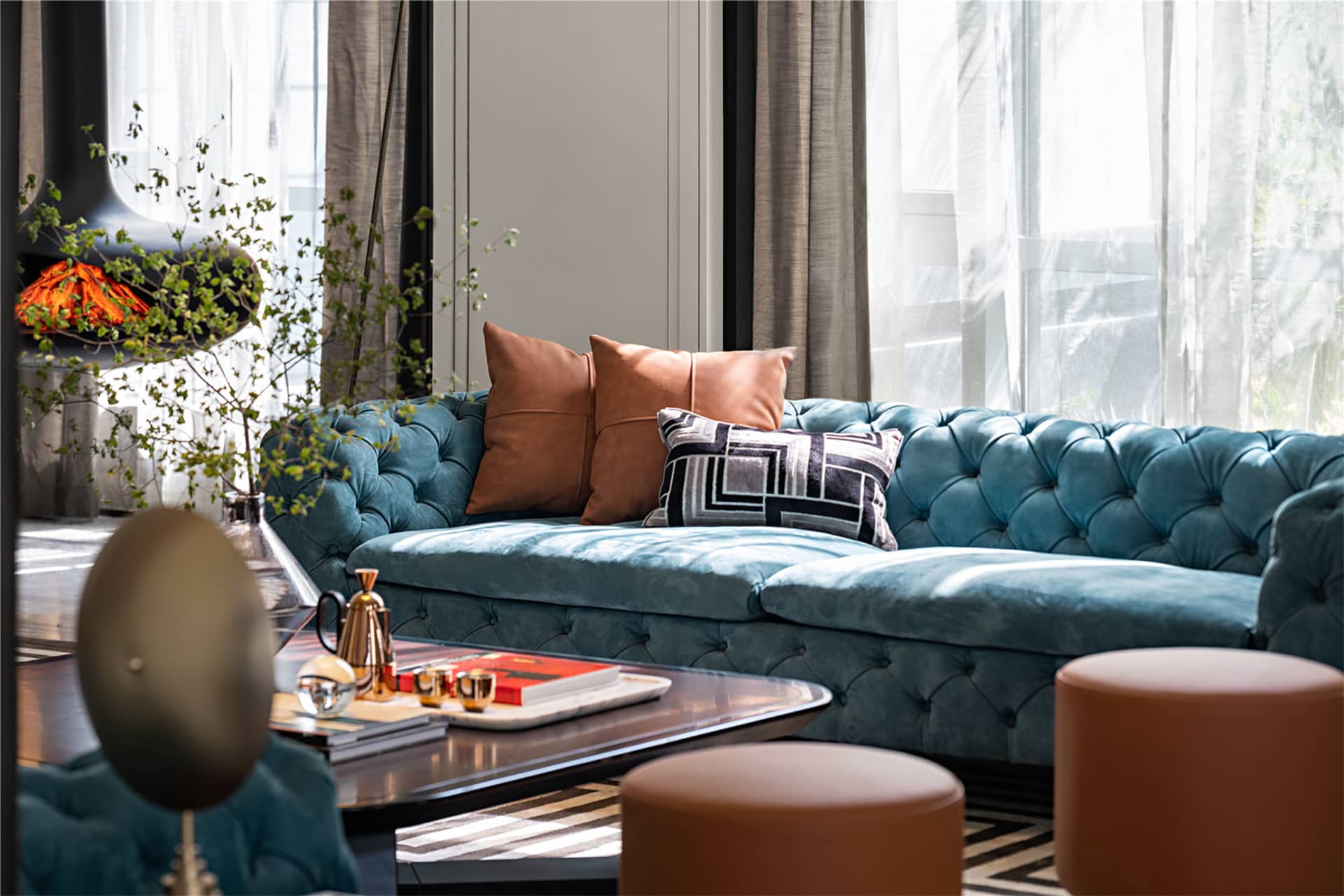 Modern living room featuring a blue tufted velvet sofa, brown leather pillows, and a wooden coffee table with books and a tea
