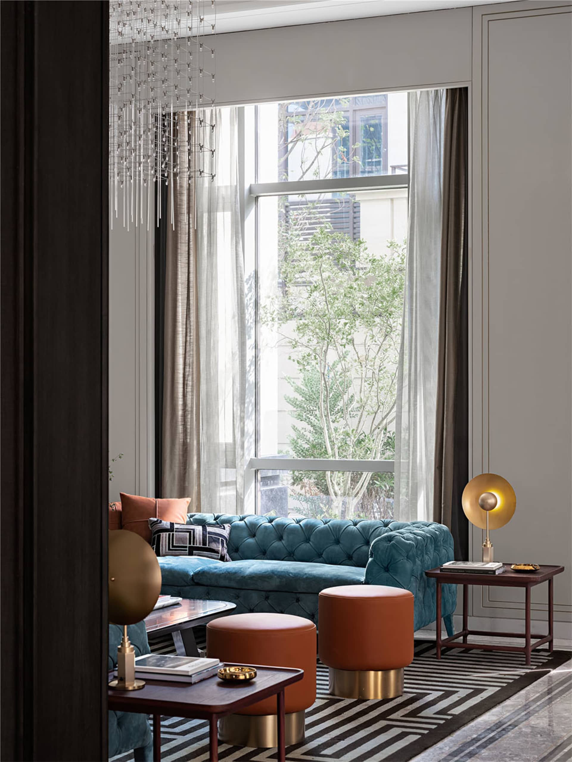 Modern living room featuring a teal fabric couch, glass chandelier, and wooden furniture.
