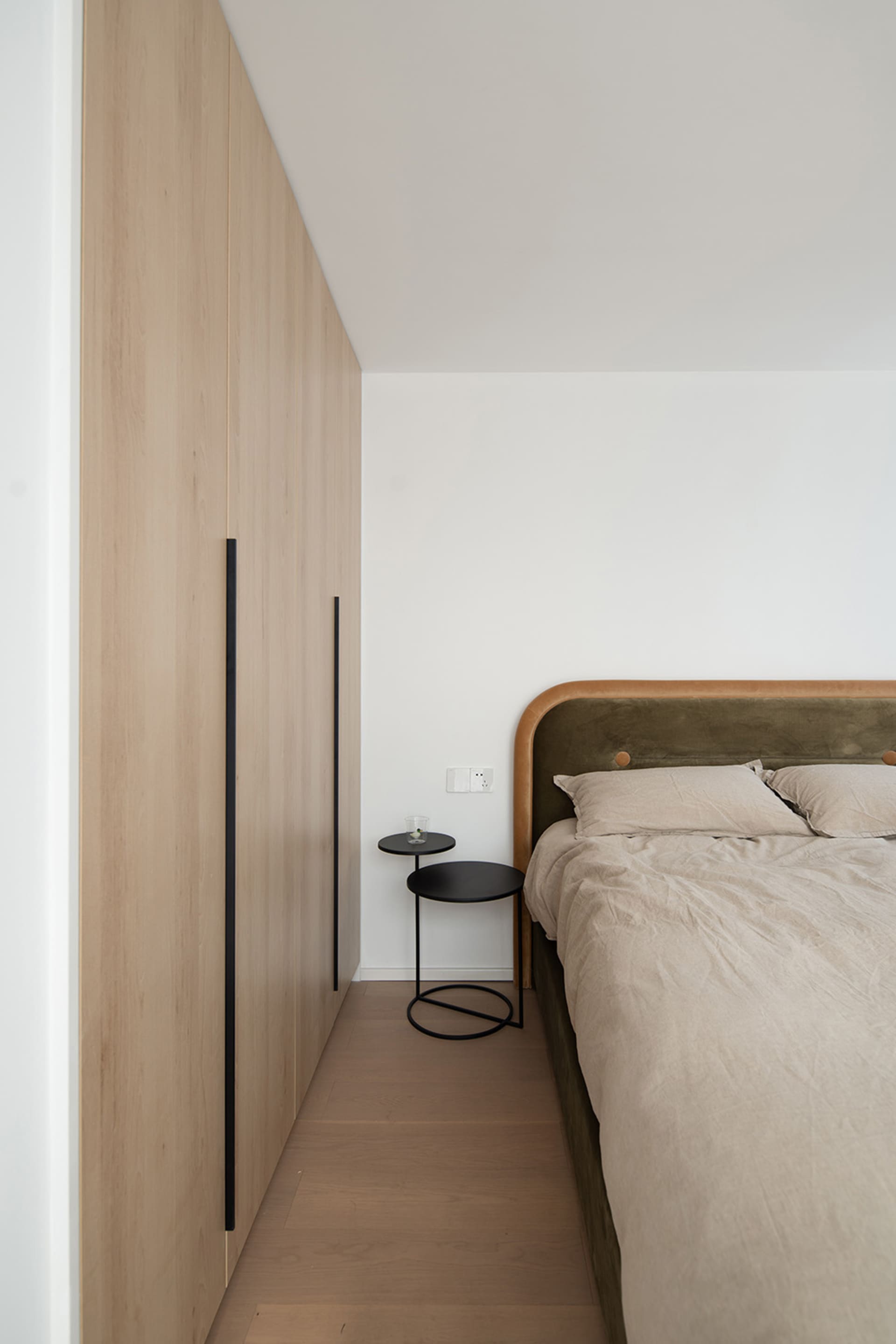 A minimalist bedroom with a wooden bed frame, side tables, and a wall-mounted wardrobe