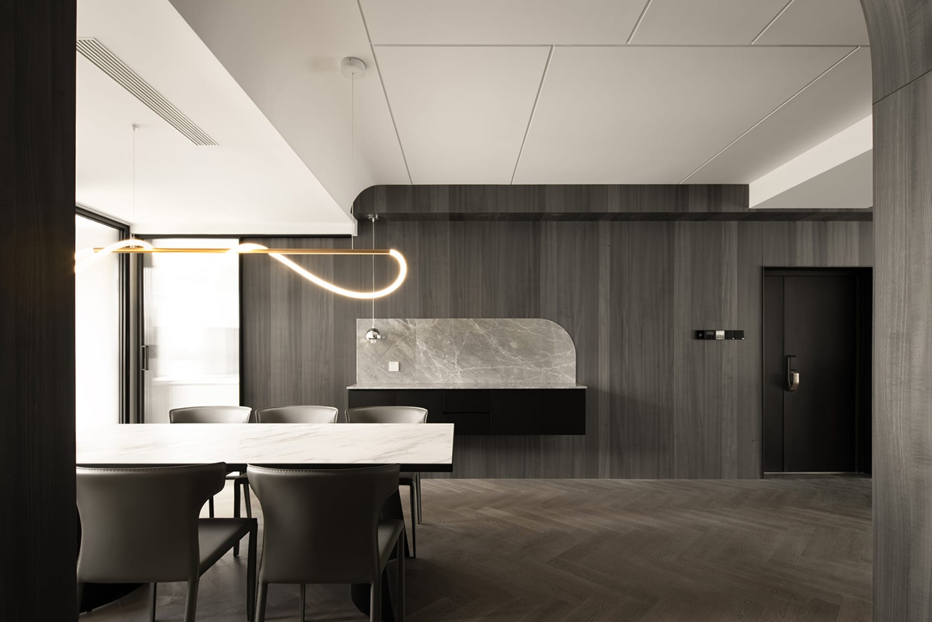 Contemporary kitchen with marble countertops and dark wooden walls, featuring a unique pendant light fixture.