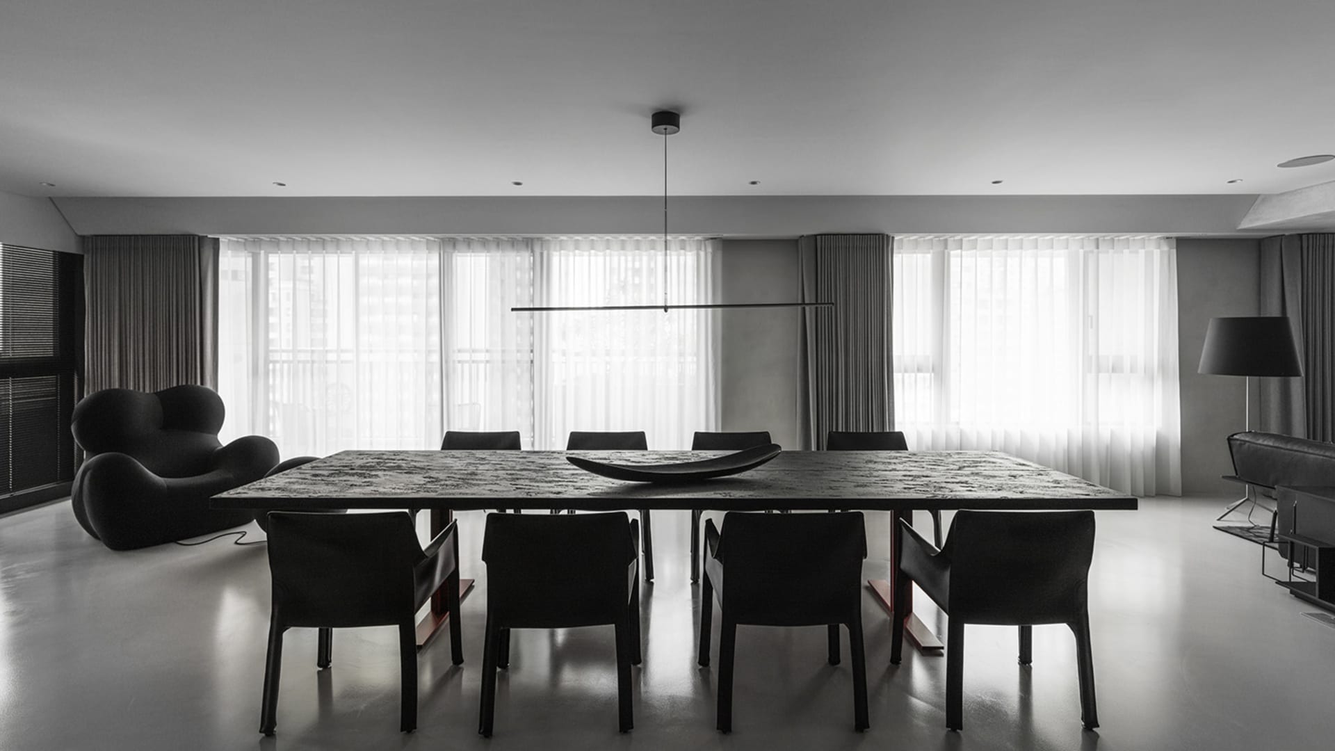A sleek, minimalist modern dining room with a long black dining table and black chairs, featuring a long black horizontal lig