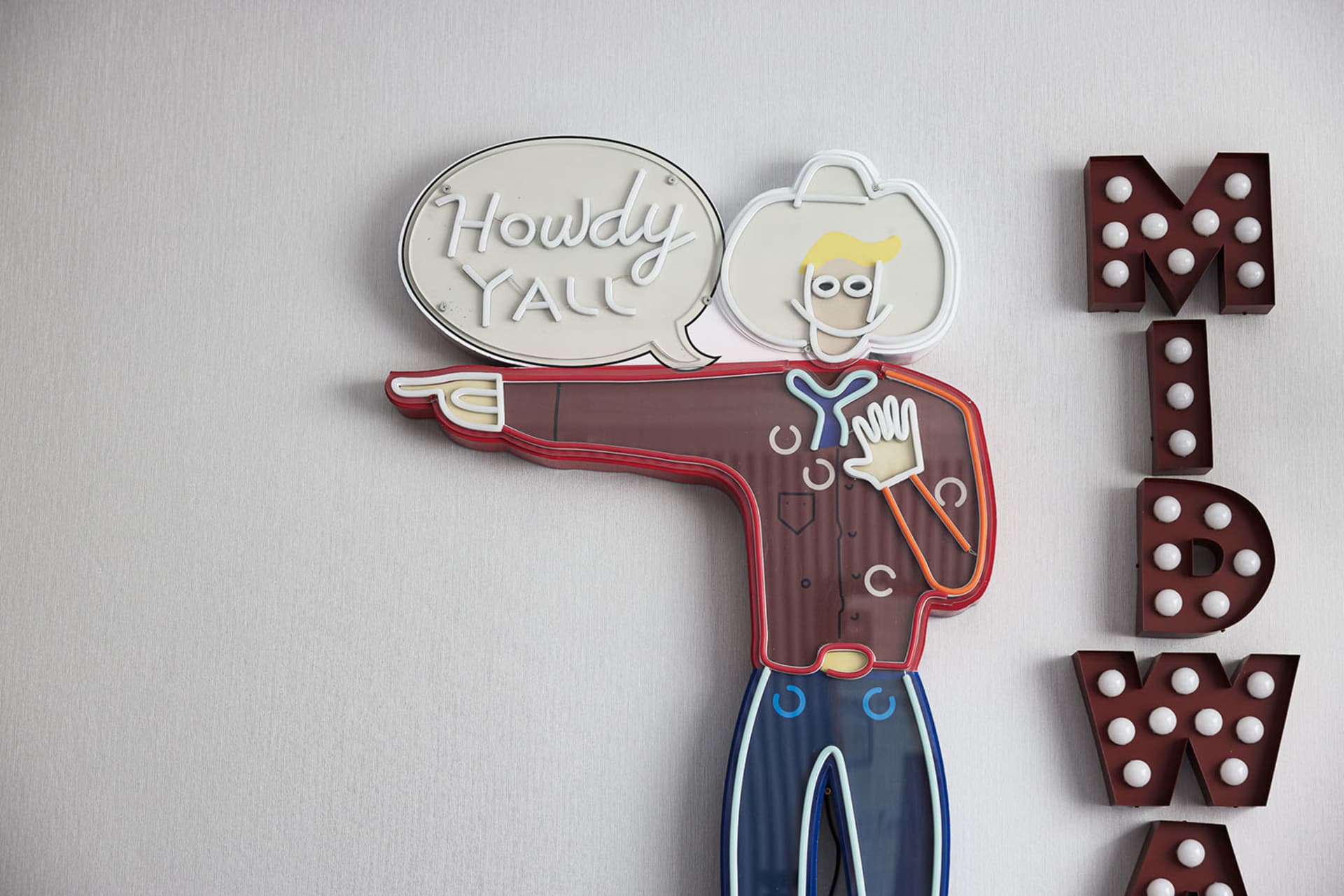A neon sign featuring a cowboy with a speech bubble saying 'Howdy Y'all'.
