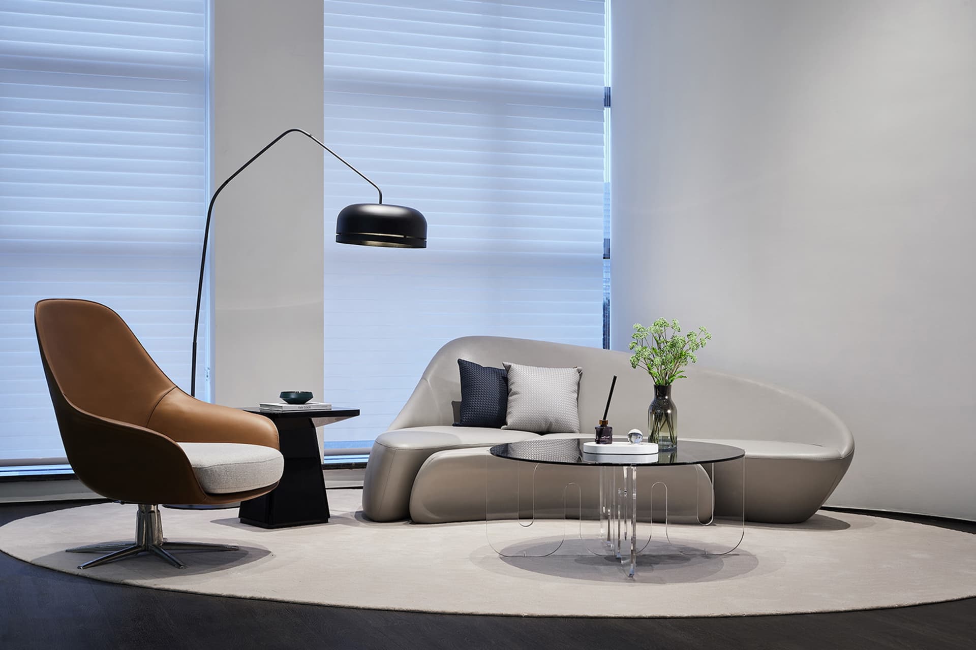 A modern living room featuring a curved leather sofa, a glass coffee table, and a sleek metal floor lamp.