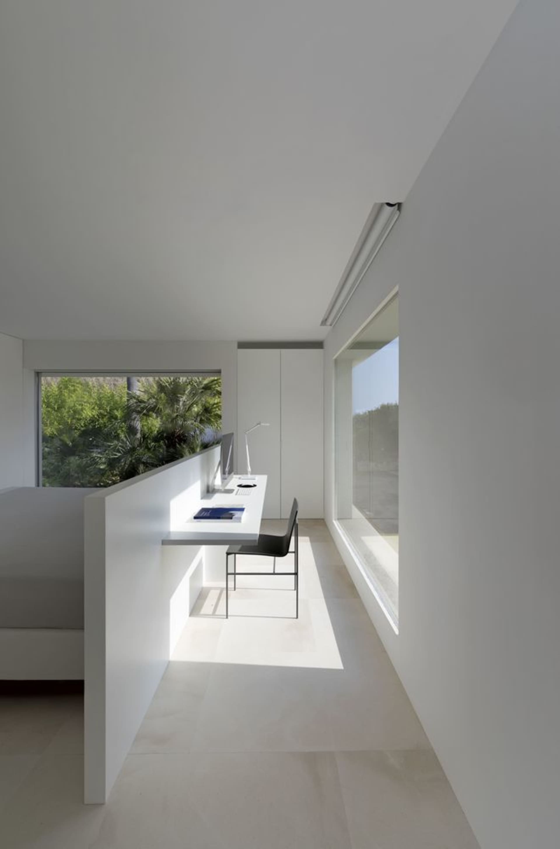 A minimalist office space in white with a desk, chair, and window.