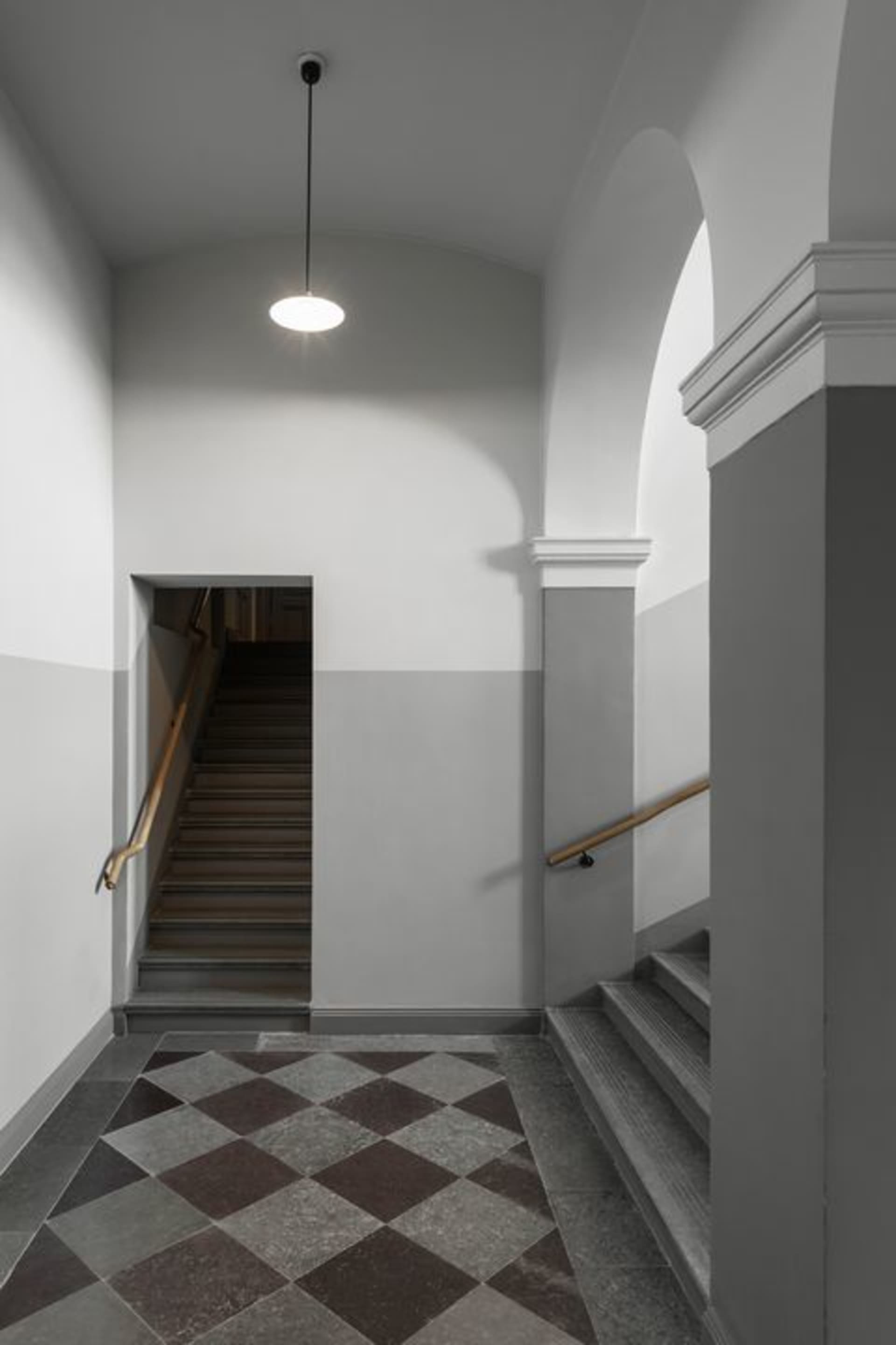 A modern interior corridor featuring concrete walls, marble stairs, and hanging light fixtures.