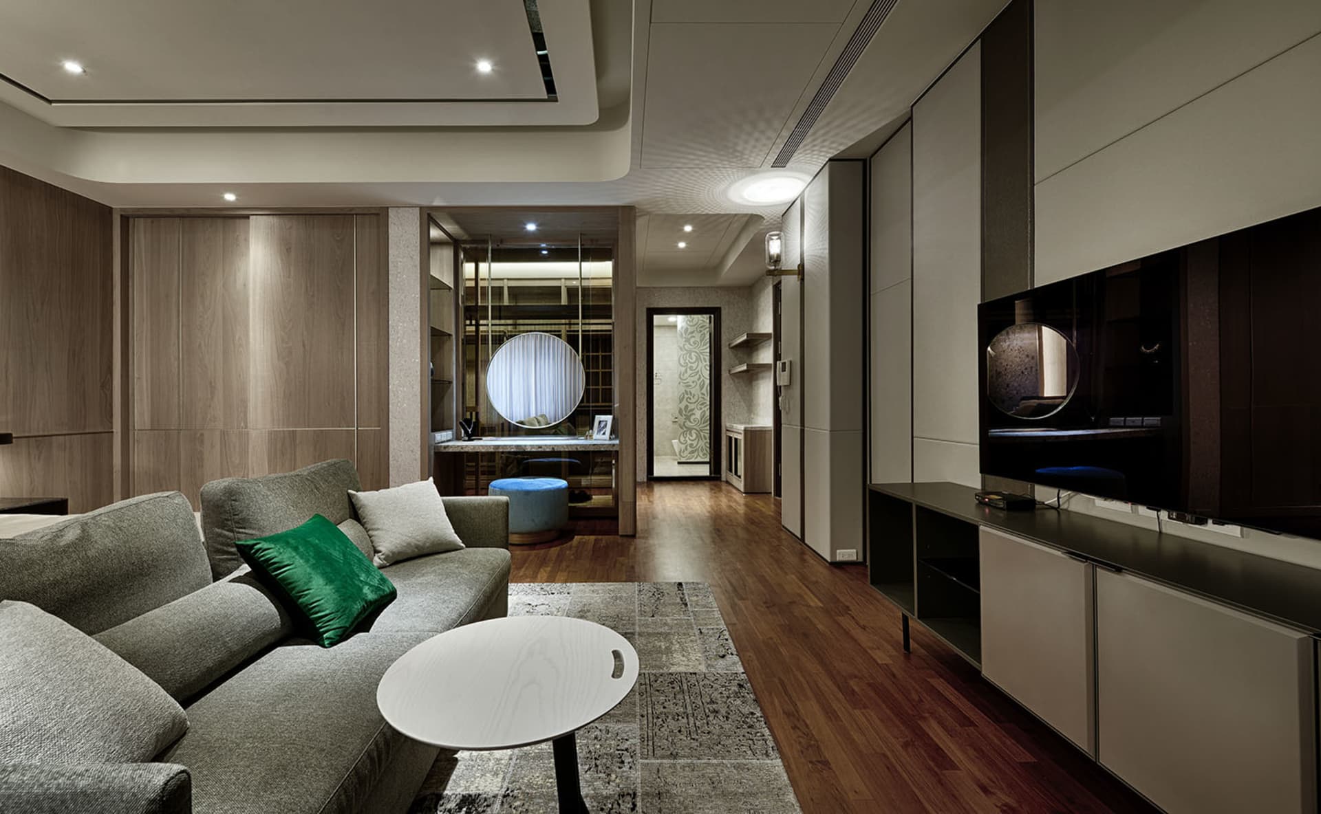 A modern apartment living room with a neutral color palette featuring a gray sectional sofa and a round white coffee table.
